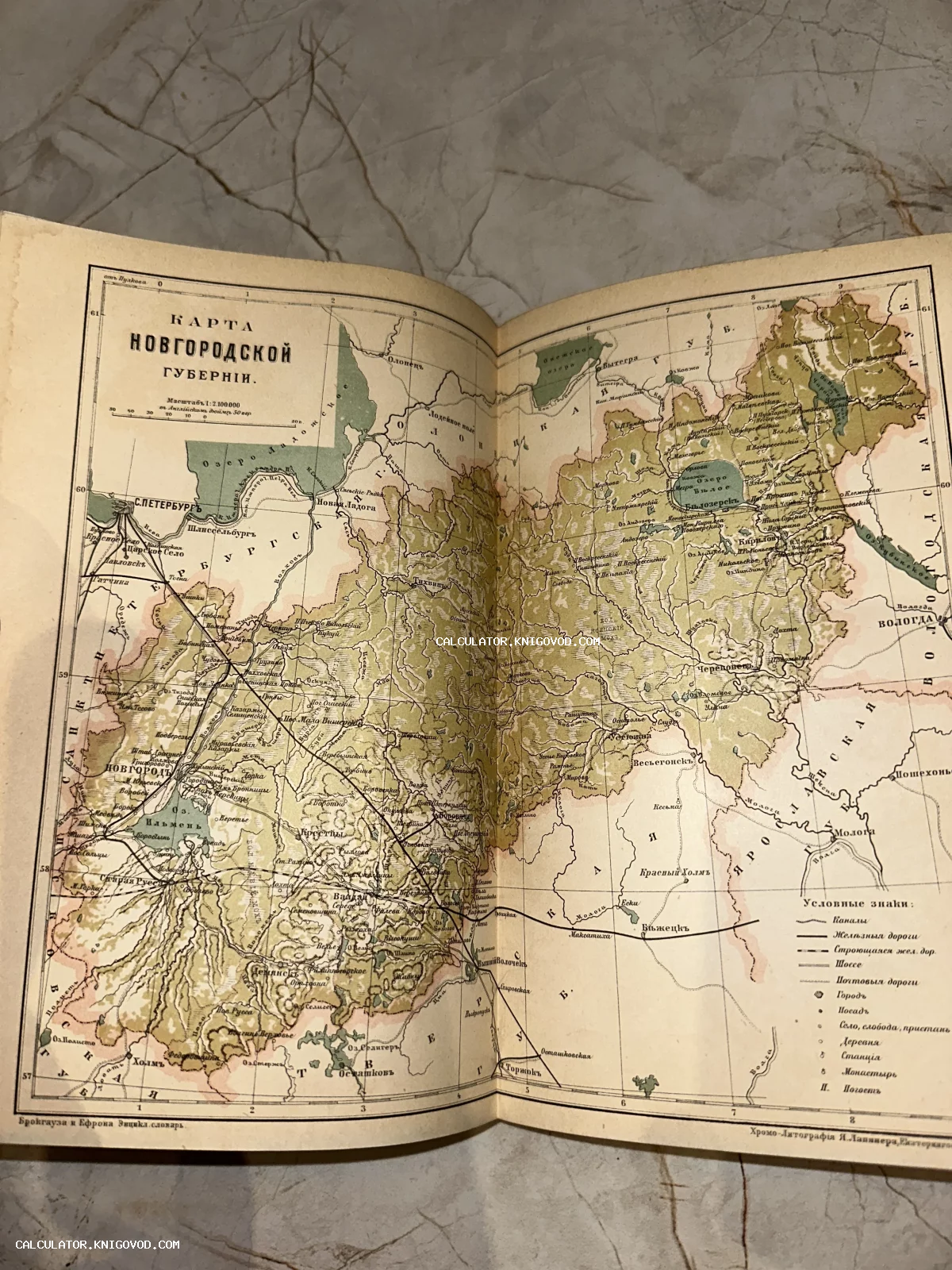 Разворот антикварного издания с подробной картой Новгородской губернии, выполненной в технике хромолитографии конца XIX века.