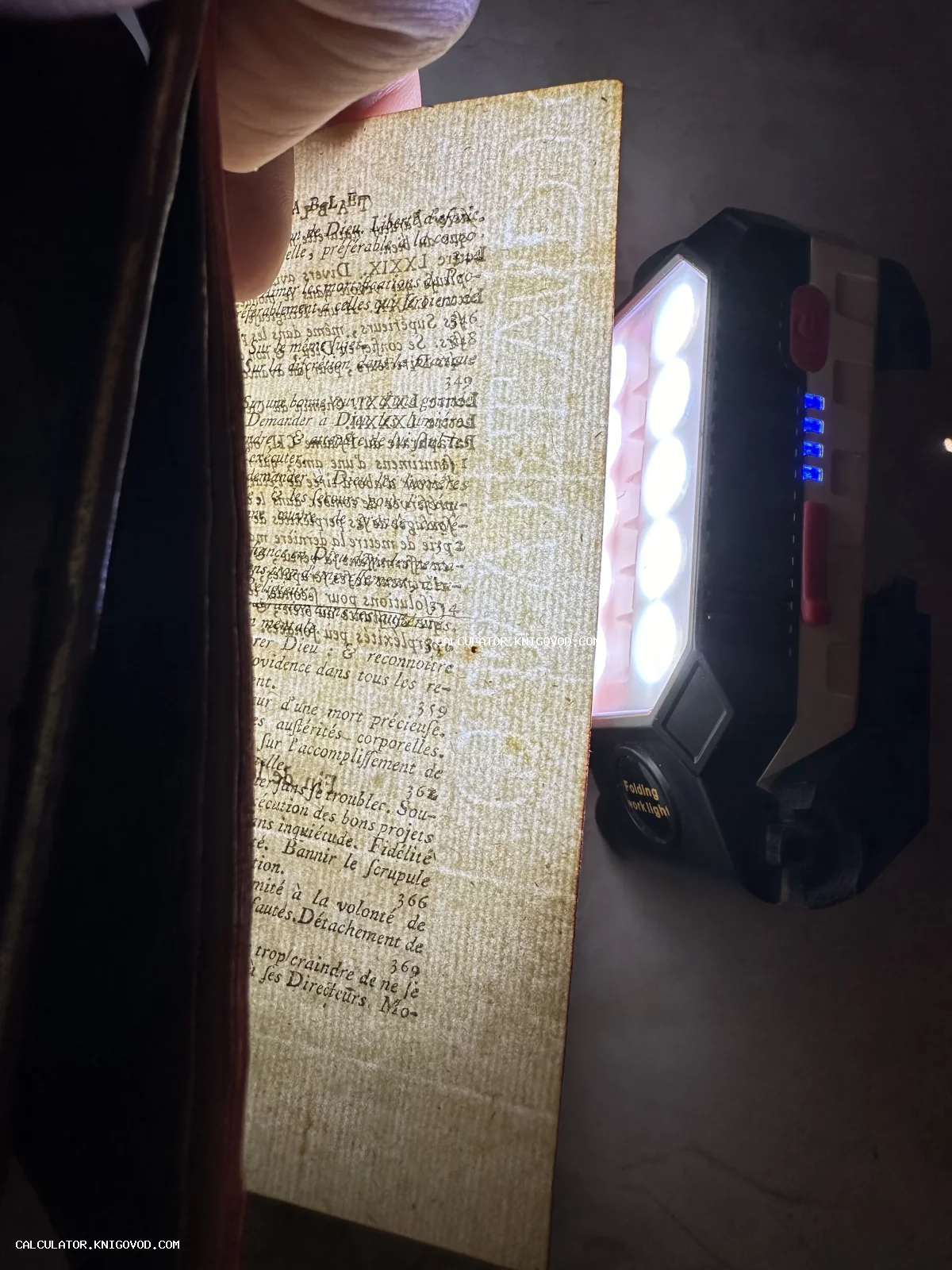 Старинная книжная страница на просвет с видимым водяным знаком и французским текстом, подсвеченная ярким фонариком.