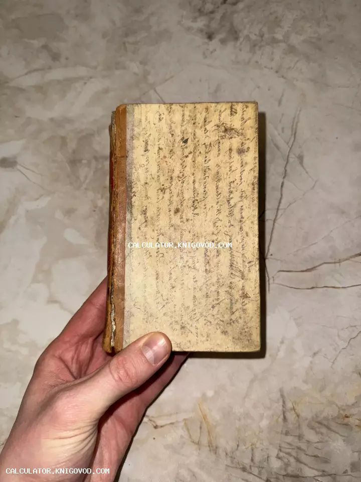 Старинная книга малого формата с рукописным текстом на обложке в руке человека на фоне мраморной поверхности.