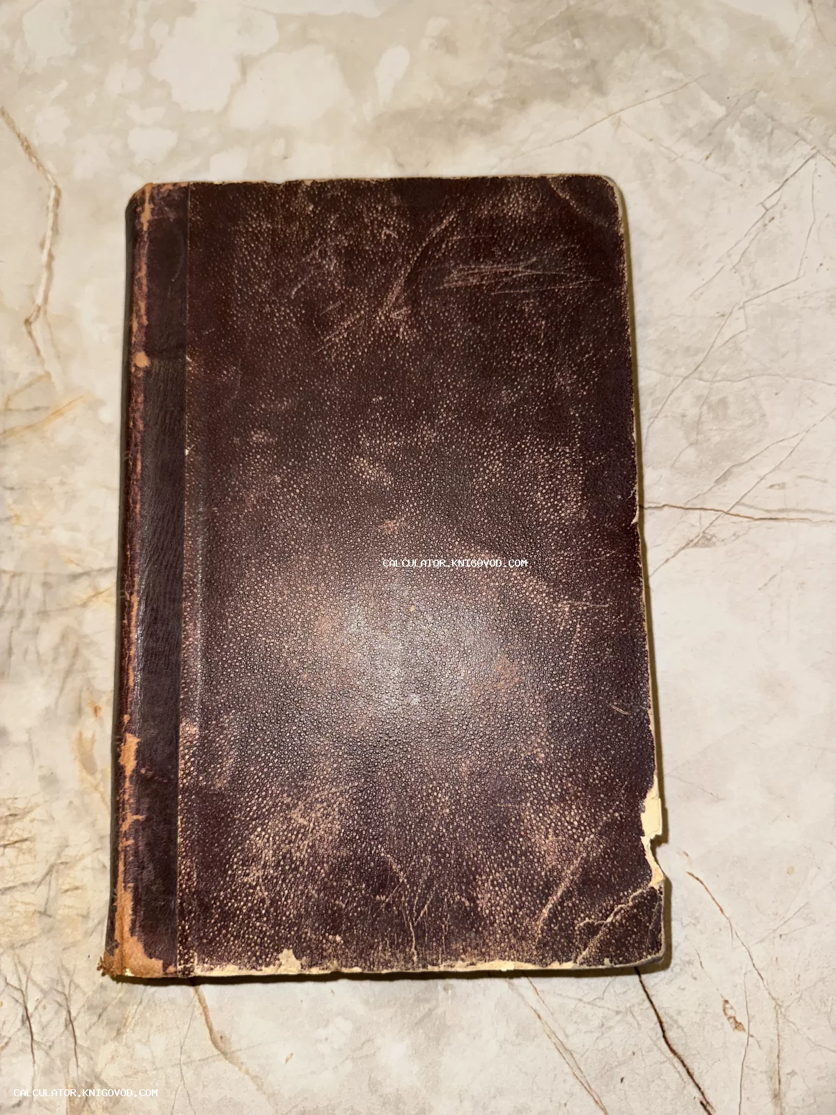 Вид сверху на старинную книгу в потертой темно-коричневой кожаной обложке, лежащую на светлой мраморной поверхности.