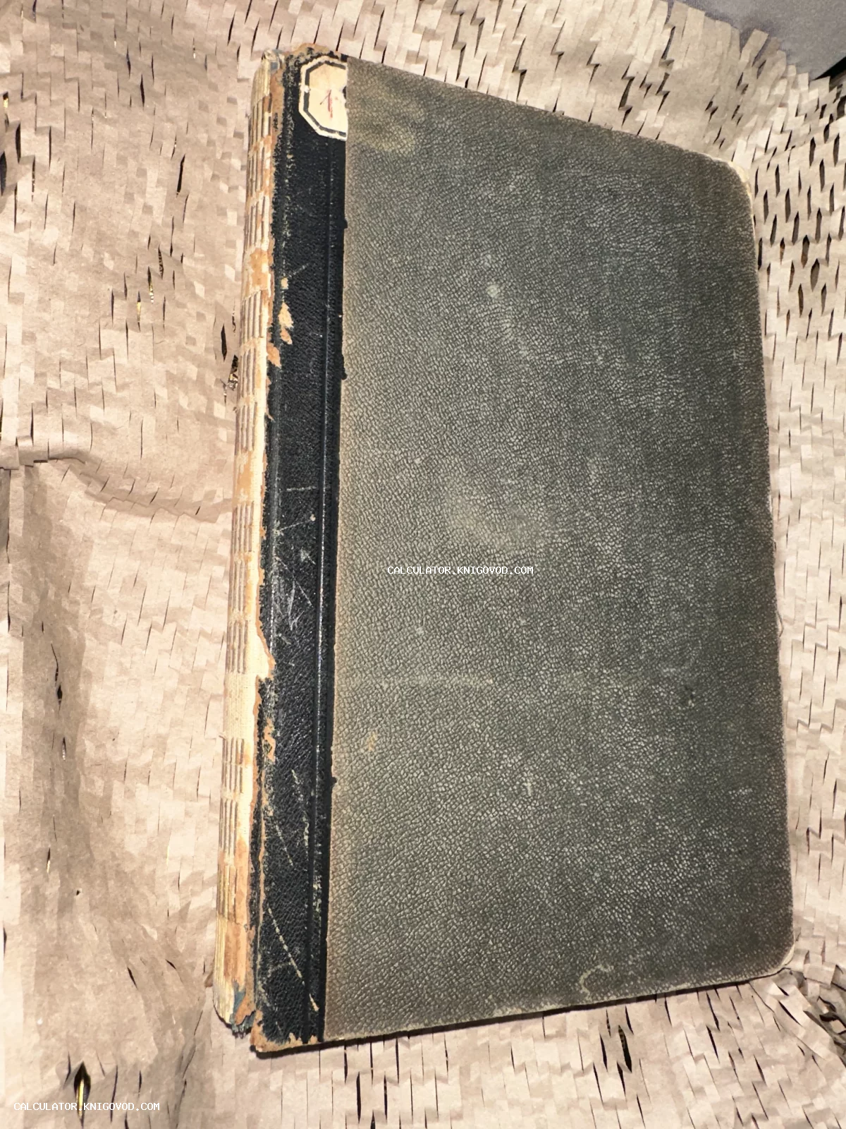 Старая антикварная книга с потертым черным корешком и серой текстурированной обложкой на упаковочной бумаге.