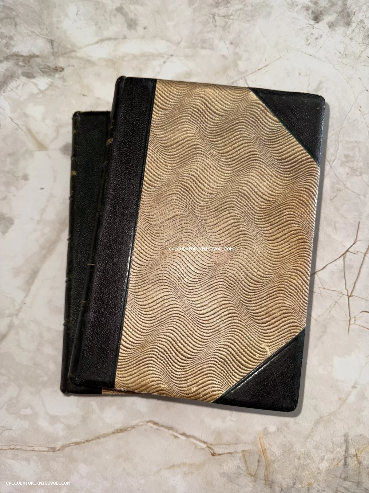 Старинная книга с темным кожаным корешком и узорчатой бумагой на обложке, лежащая на мраморной поверхности