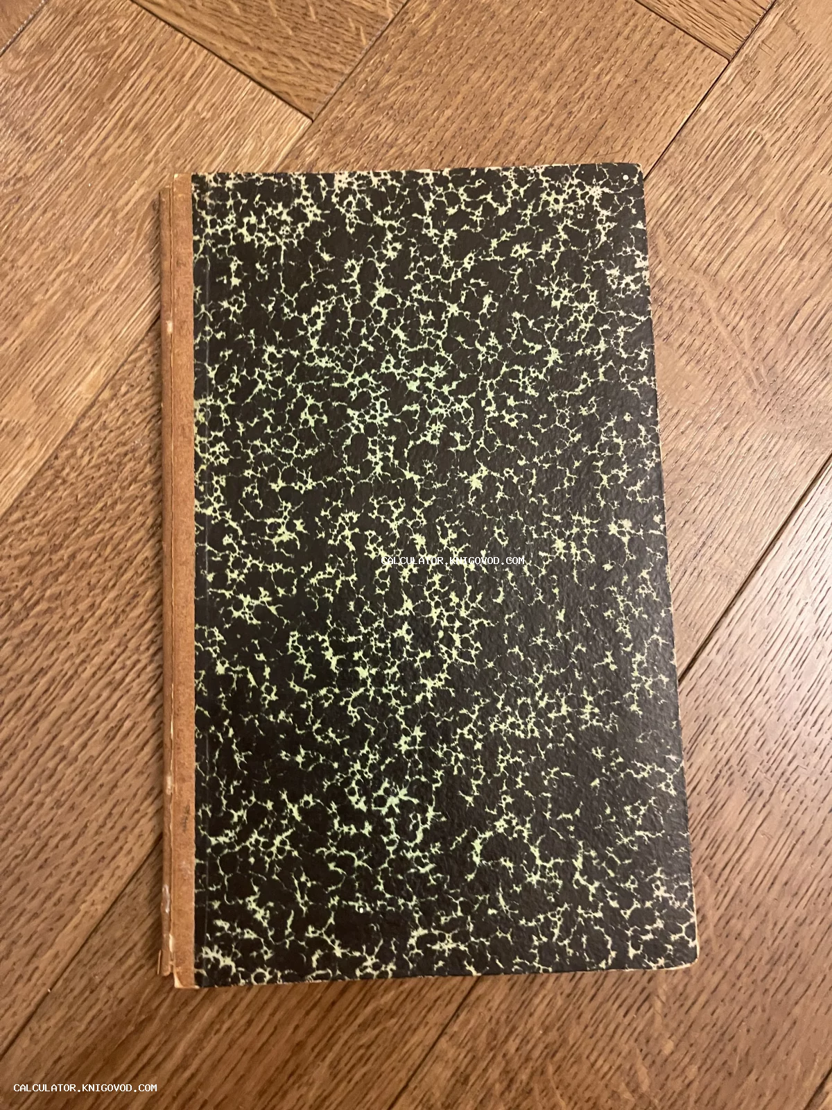 Старинная книга с темно-зеленой обложкой с мраморным узором и коричневым корешком на деревянном полу.