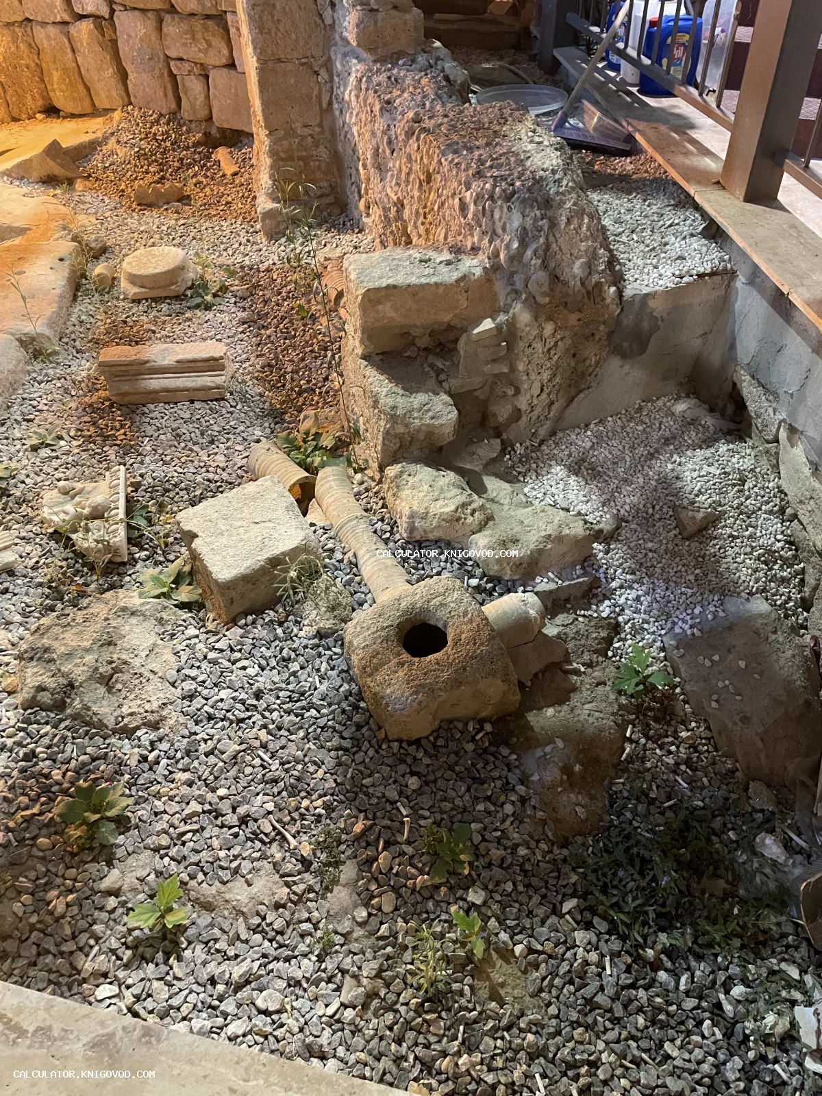 Археологические раскопки с каменной кладкой, блоками и элементами древнего водопровода на гравийной засыпке.