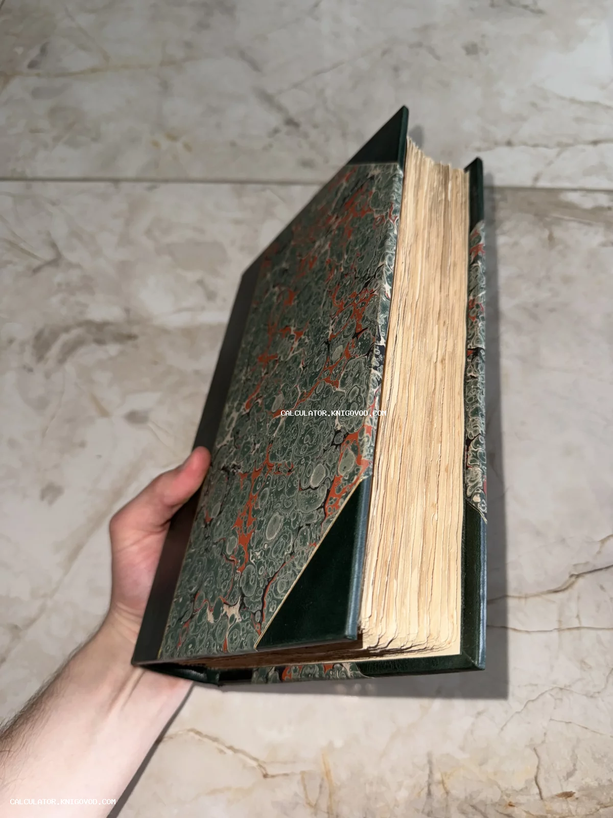 Старинная книга с обложкой из мраморной бумаги и кожаными вставками в руке человека