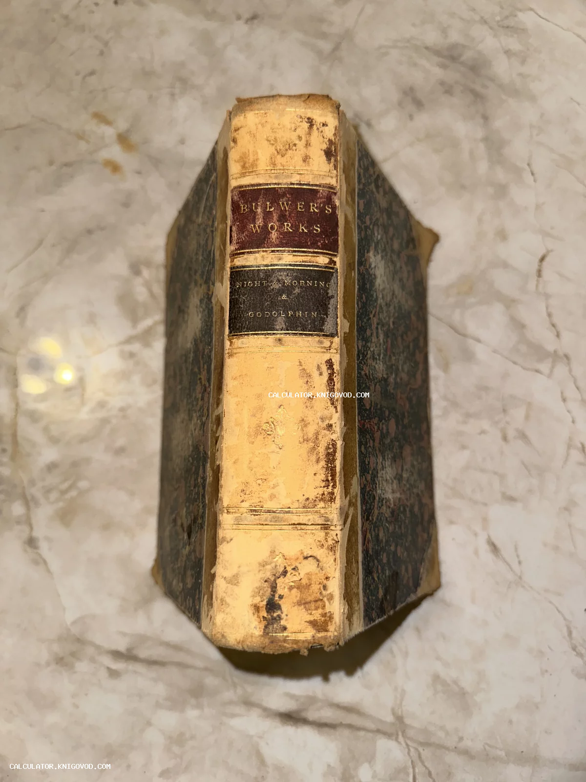 Старинный кожаный корешок книги Эдварда Бульвер-Литтона с золотым тиснением на мраморной поверхности.