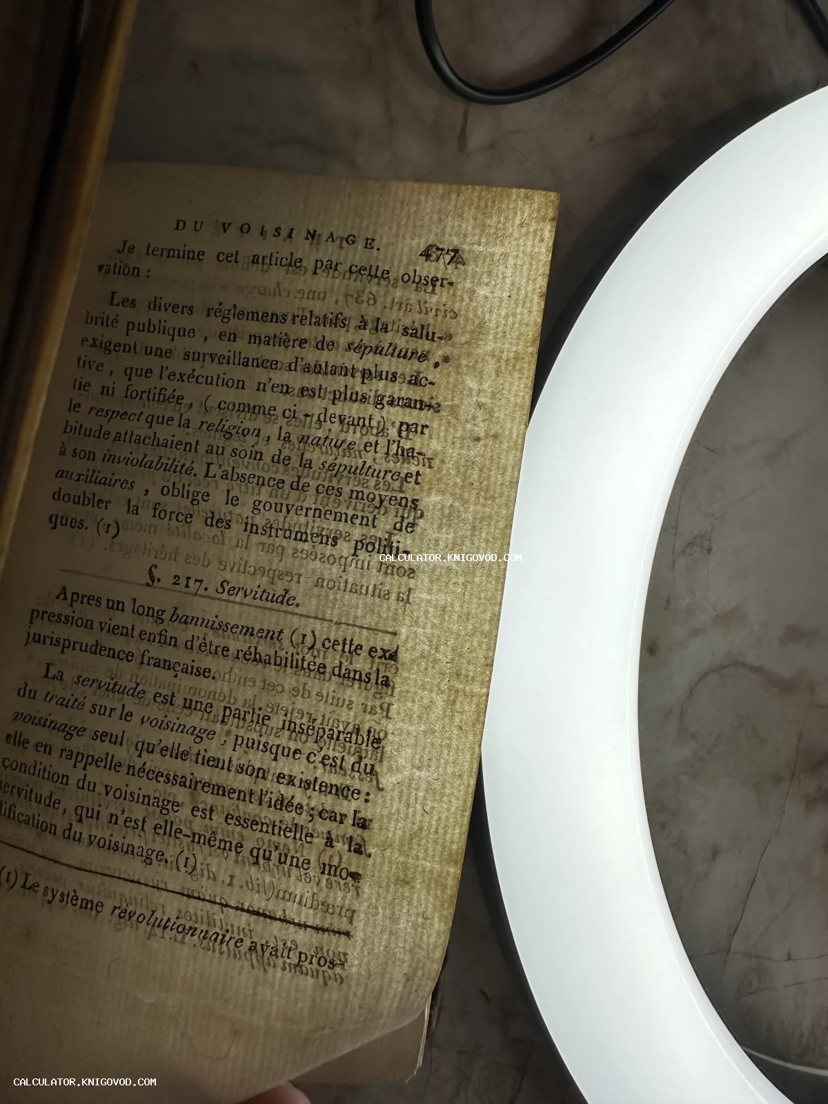 Пожелтевшая страница антикварной книги на французском языке с заголовком DU VOISINAGE под светом лампы.