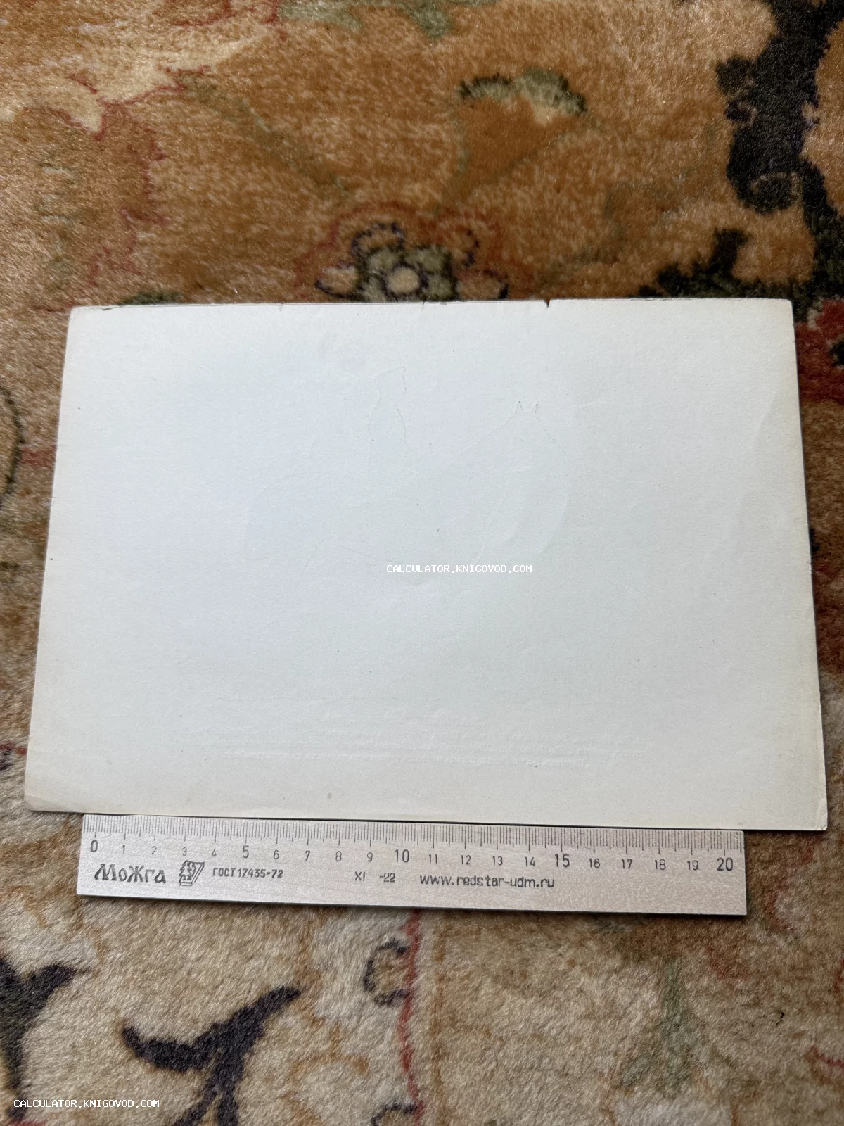 Оборотная сторона чистой старинной открытки с едва заметным рельефным тиснением в виде всадника на лошади, под которой лежит измерительная линейка.