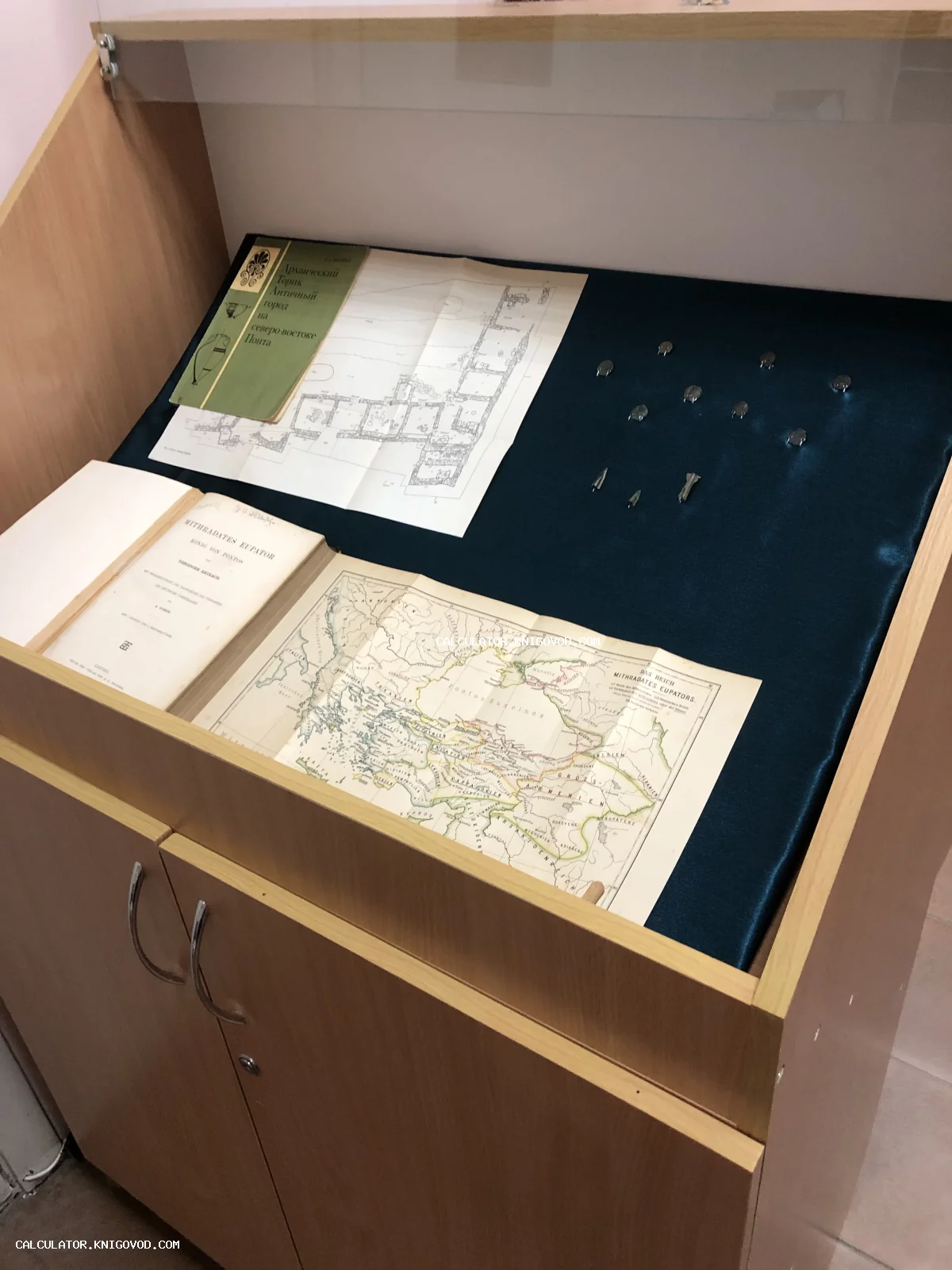 Музейная витрина с антикварной книгой о Митридате Евпаторе, развернутой исторической картой Понтийского царства и археологическим планом города Торик.