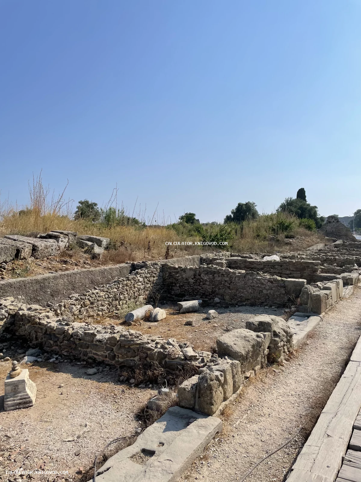 Археологические раскопки древних каменных стен и фрагментов колонн под ясным голубым небом.