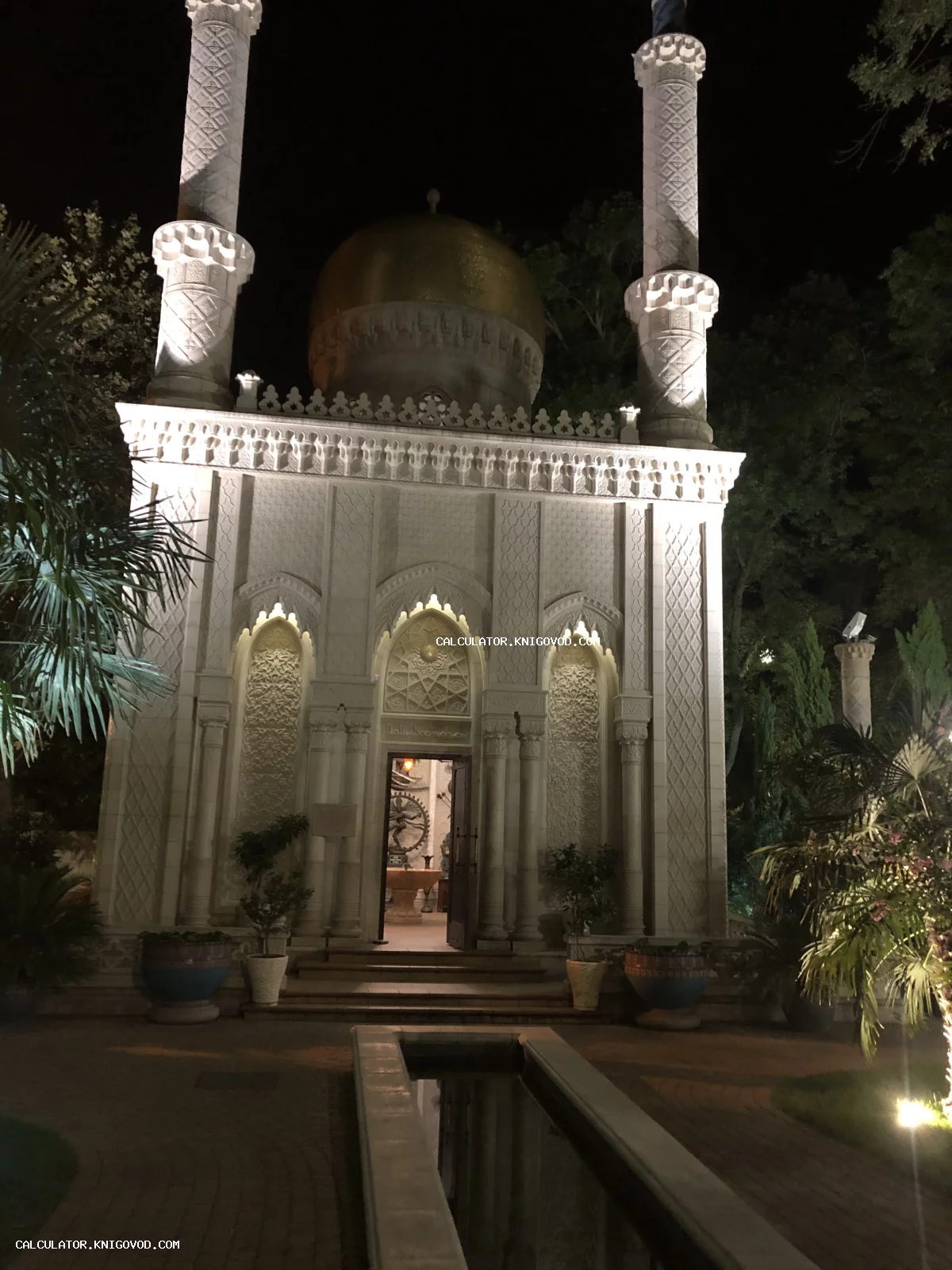 Ночной вид на здание в мавританском стиле с золотым куполом, двумя минаретами и декоративным бассейном на переднем плане.