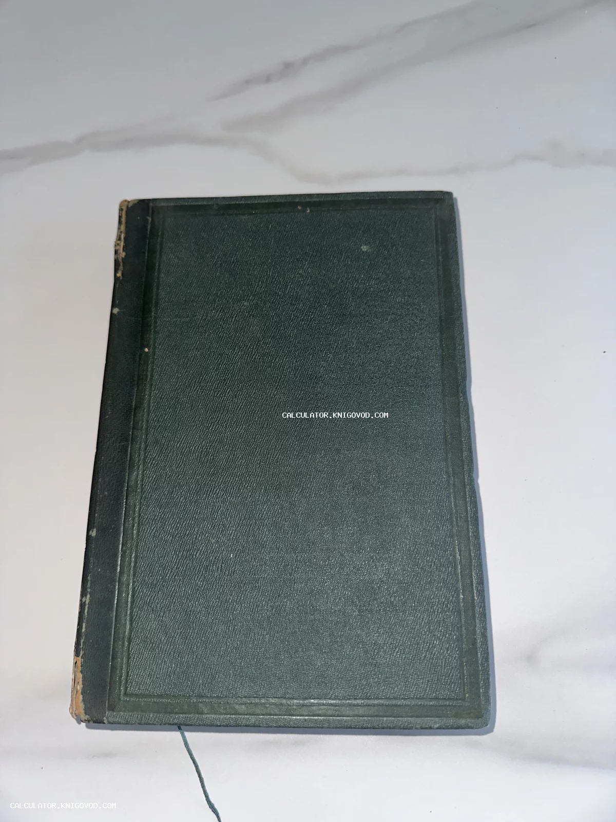 Старая книга с темно-изумрудной фактурной обложкой и черным потертым корешком на светлом мраморе.