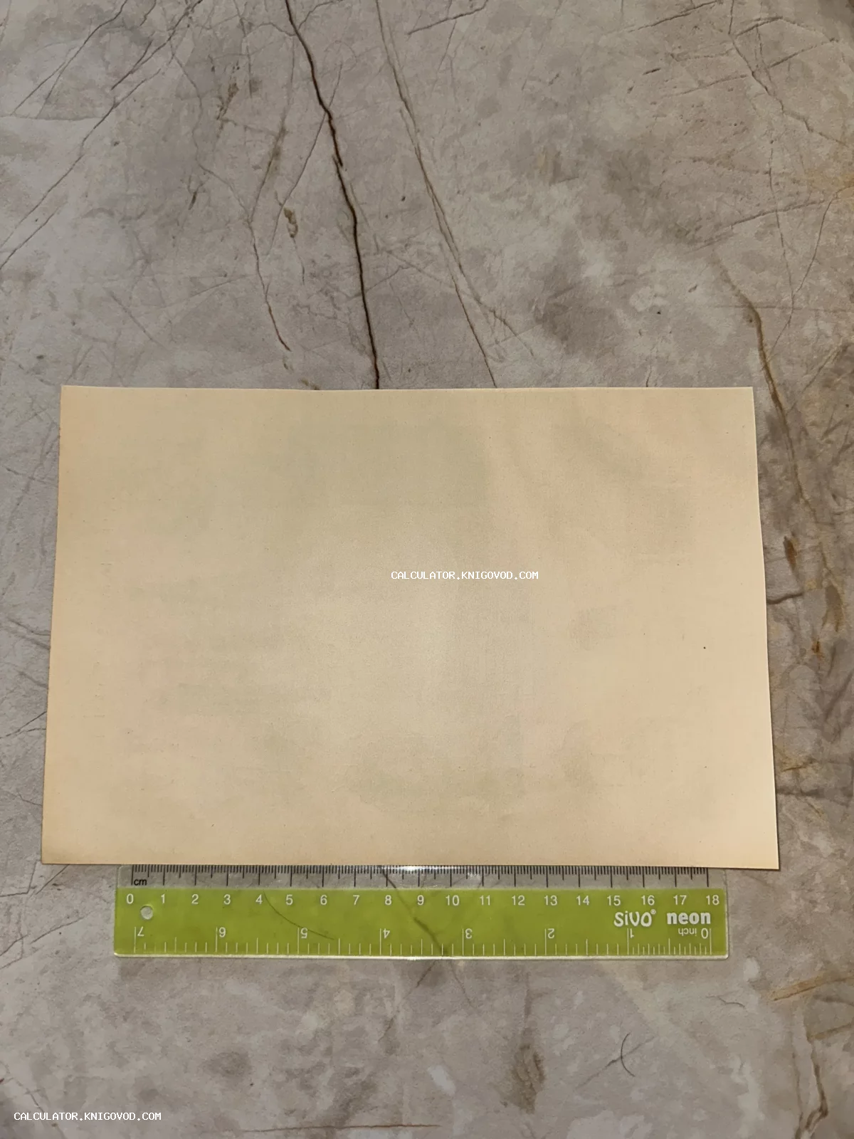 Чистая оборотная сторона старой почтовой карточки бежевого цвета на мраморном фоне с измерительной линейкой.