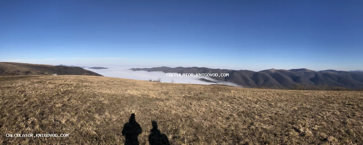 Панорамная фотография горных хребтов, погруженных в густой белый туман под ясным синим небом с тенями людей на переднем плане.