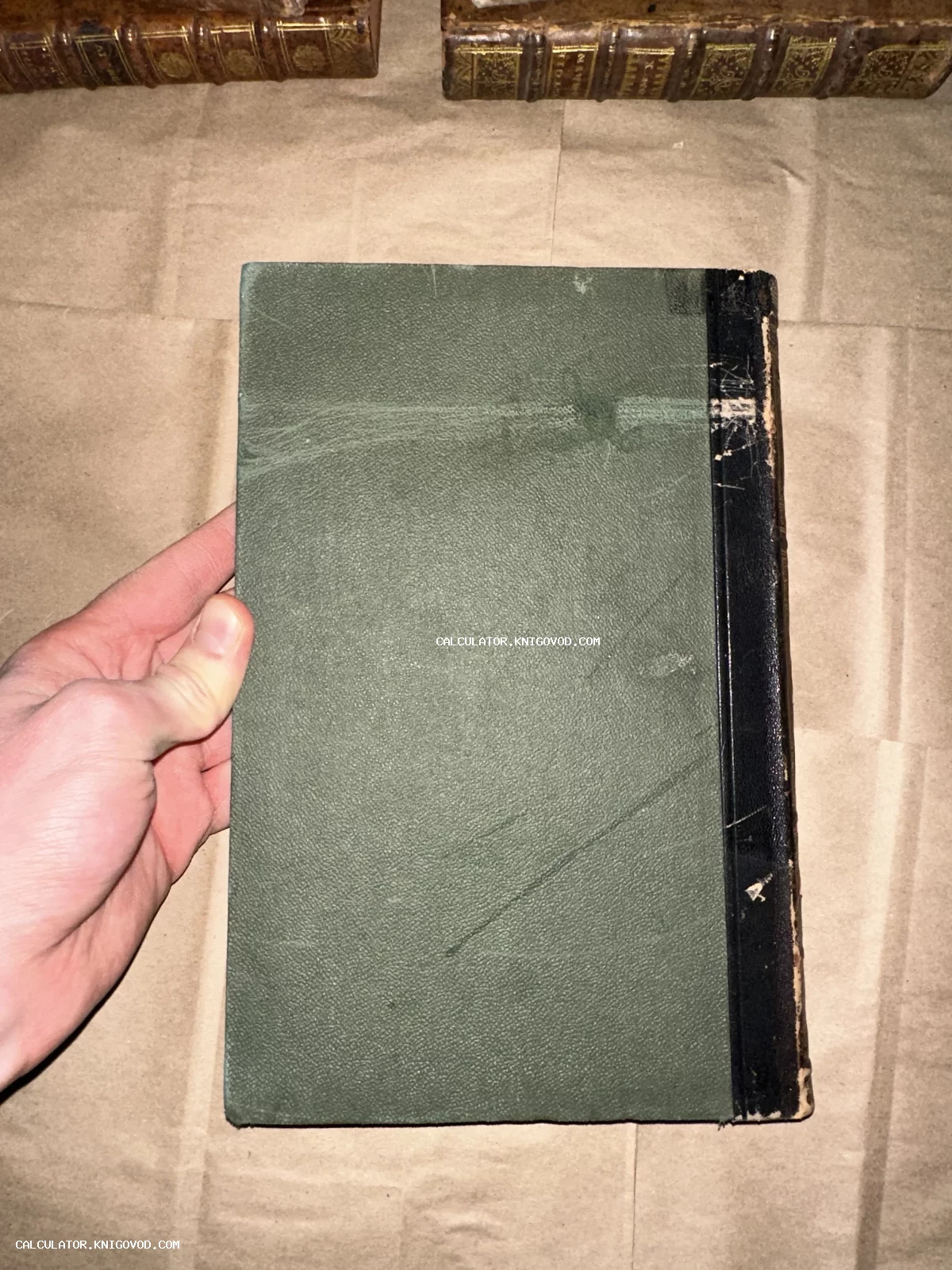 Старинная книга с зеленой фактурной обложкой и черным корешком в руках коллекционера.