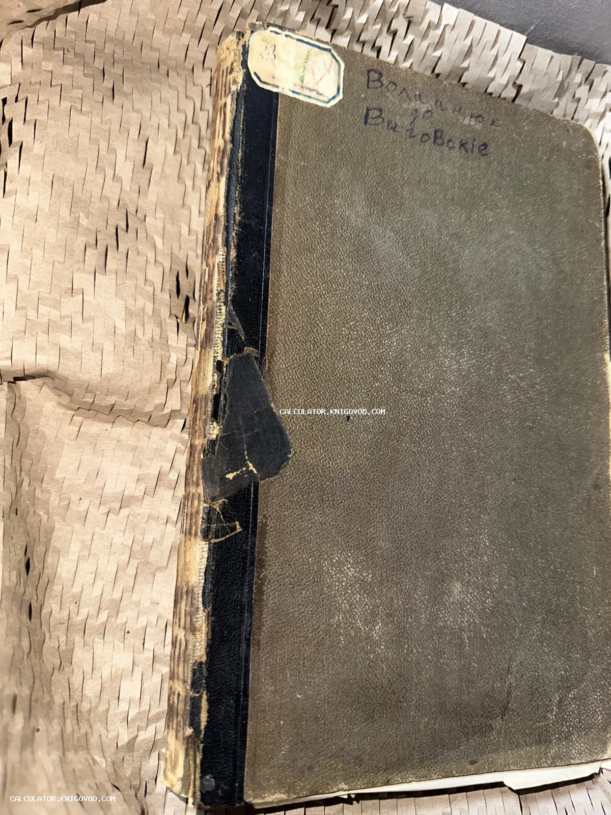 Старинная книга в потрепанном твердом переплете с поврежденным корешком и надписью от руки на обложке.