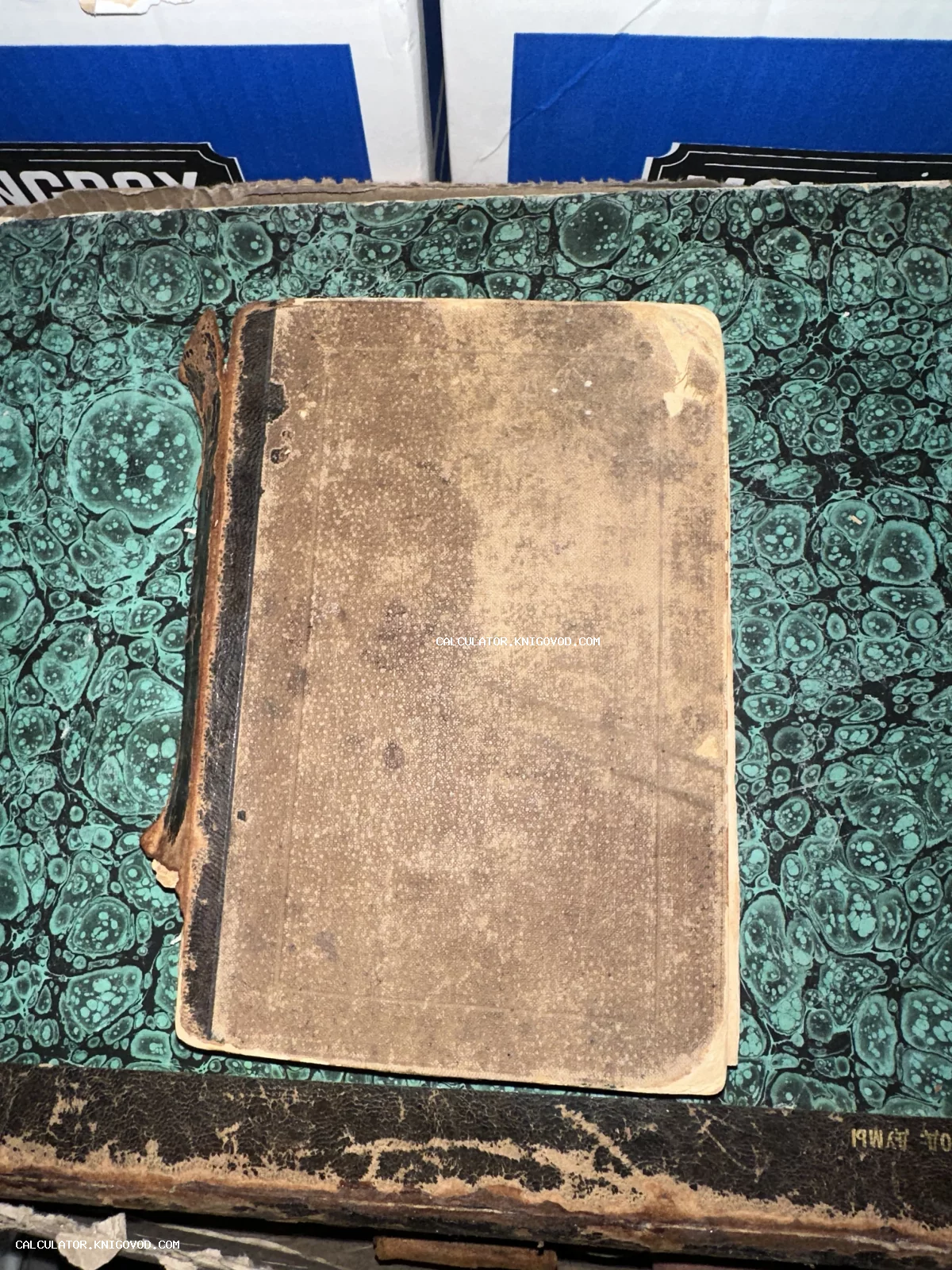Старинная книга с изношенной коричневой обложкой и темным корешком на фоне зеленой мраморной бумаги.