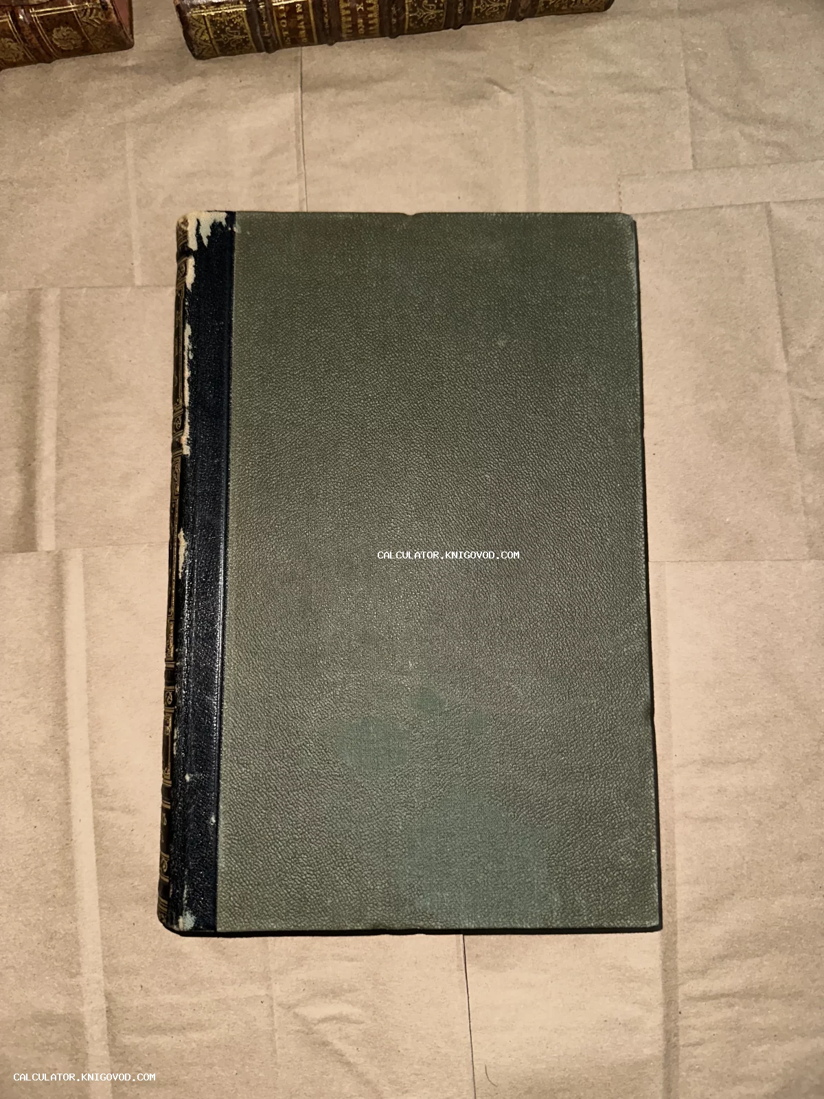 Вид сверху на антикварную книгу с темно-зеленой текстурированной обложкой и потертым темным корешком.