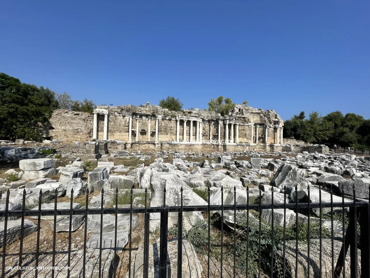 Панорамный вид на руины античного здания с белыми мраморными колоннами и россыпью камней под ярко-синим небом.