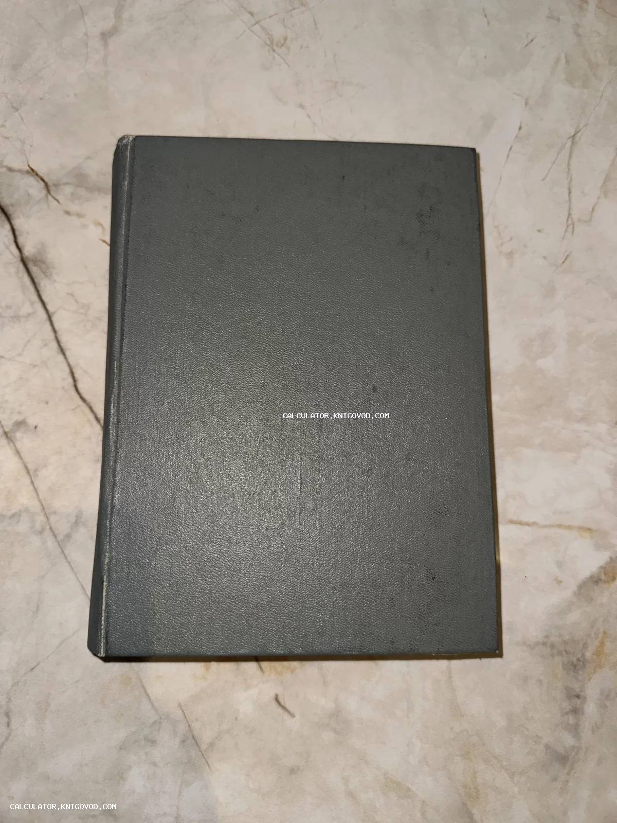 Вид сверху на закрытую старинную книгу в сером твердом переплете с текстурой, лежащую на светлой мраморной поверхности.