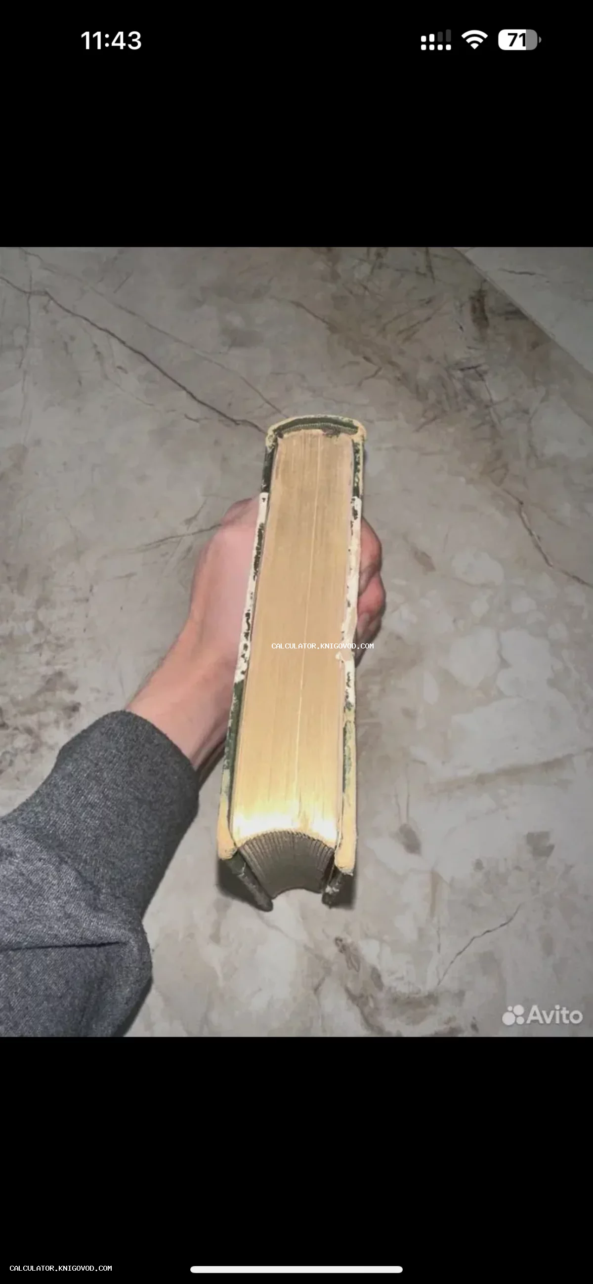 Вид сверху на обрез пожелтевших страниц и потертую обложку старинной книги в руке человека.