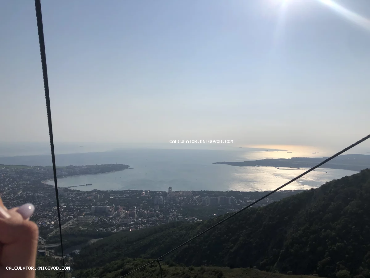 Вид на прибрежный город и дугообразную бухту с горного склона при ярком солнечном свете.