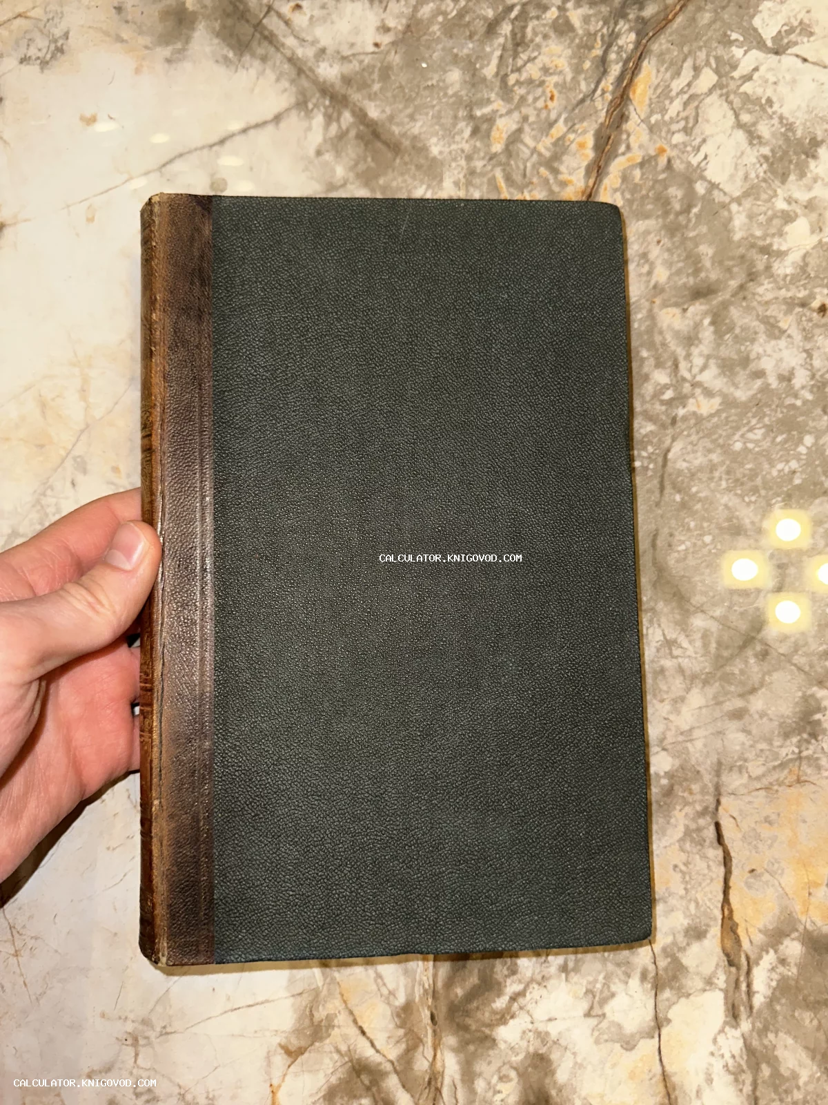 Старинная книга с темно-зеленой фактурной обложкой и потертым коричневым кожаным корешком на фоне мрамора