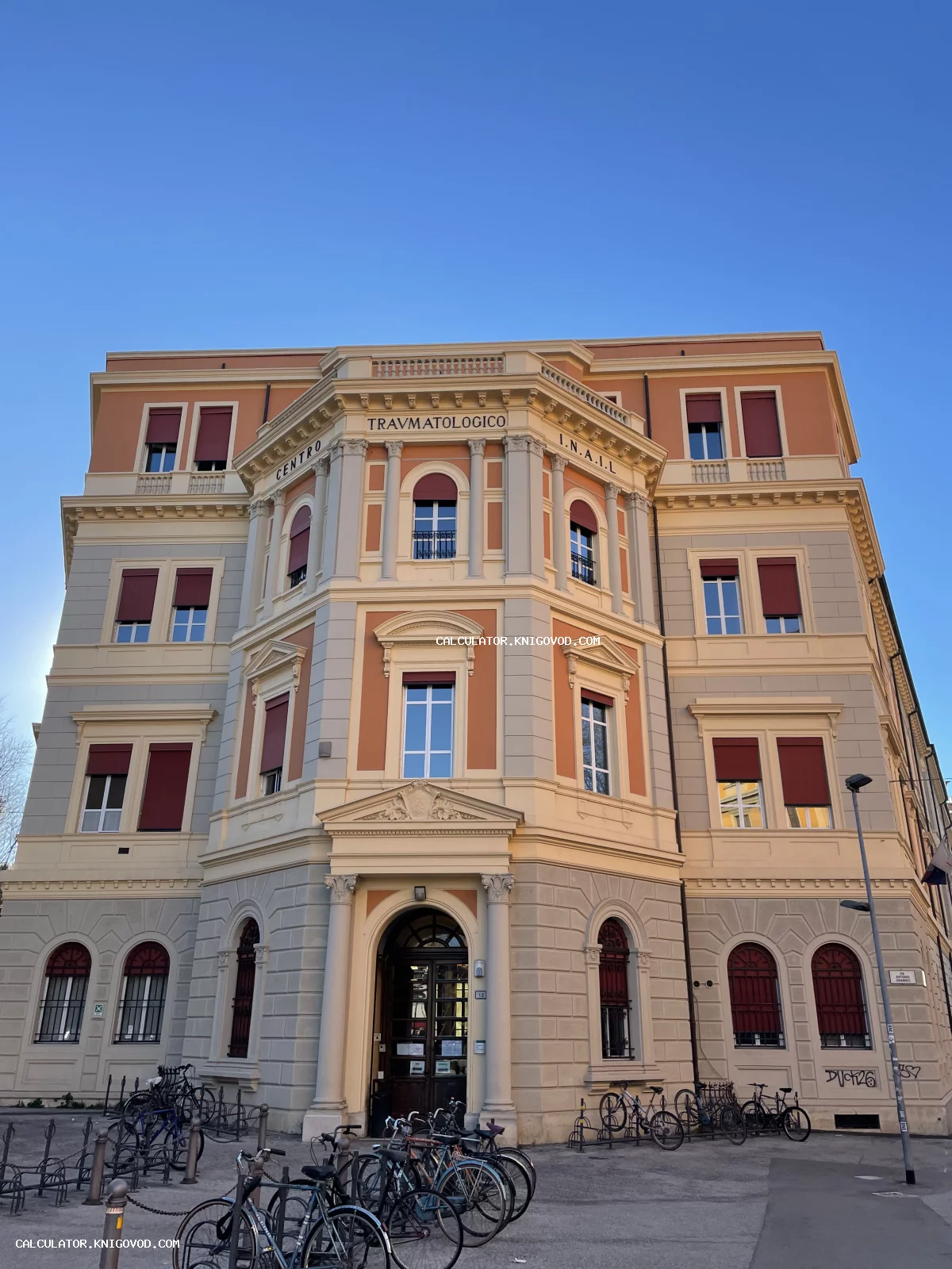 Фасад многоэтажного здания в неоклассическом стиле с надписью Centro Traumatologico I.N.A.I.L. и велосипедной парковкой перед входом.