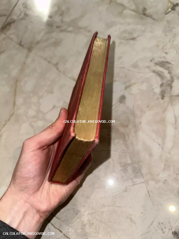 Рука держит старинную книгу в красном переплете с позолоченным обрезом страниц