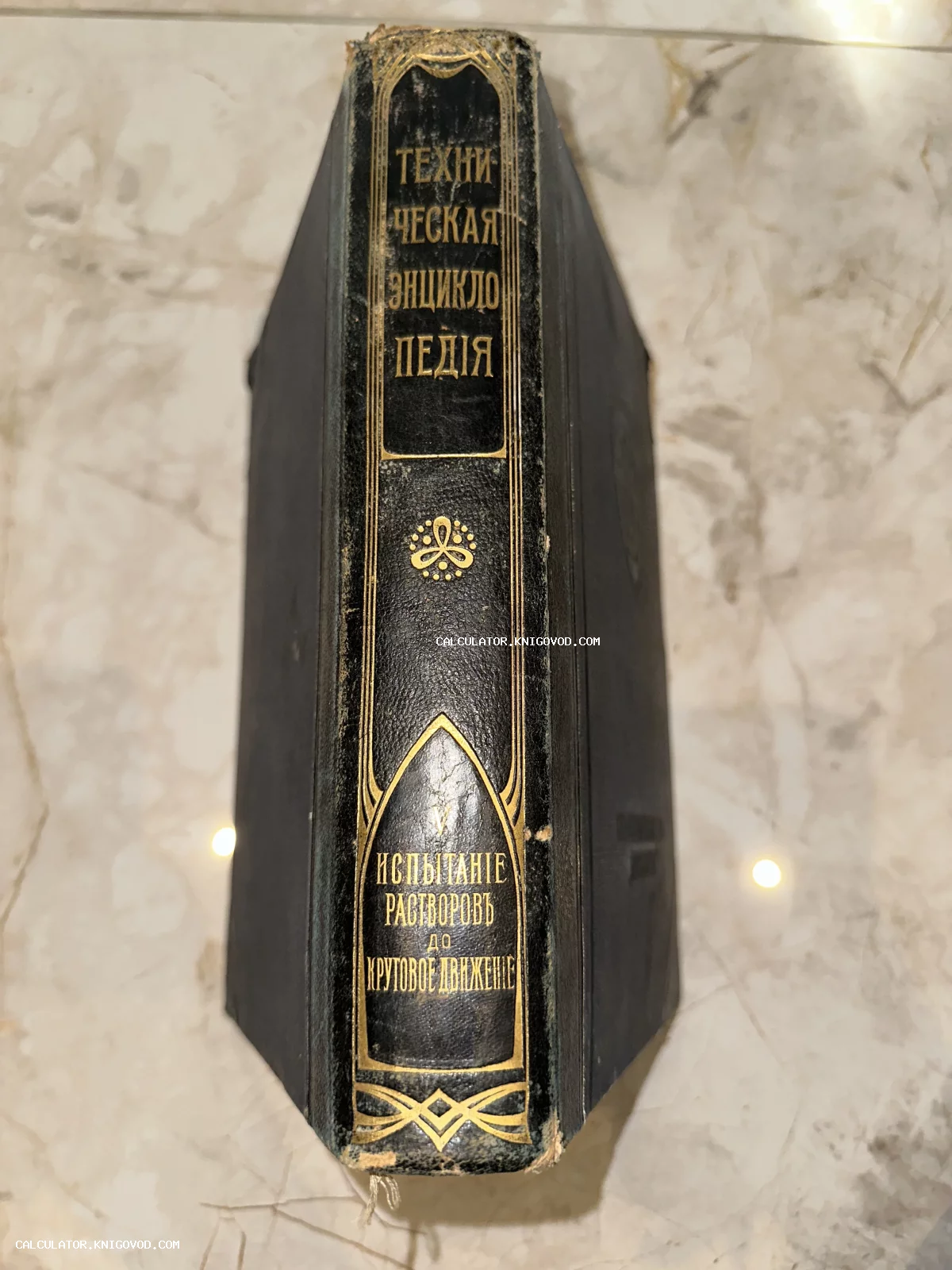 Корешок старинной книги с золотым тиснением «Техническая энциклопедия», том 5, на мраморном фоне.