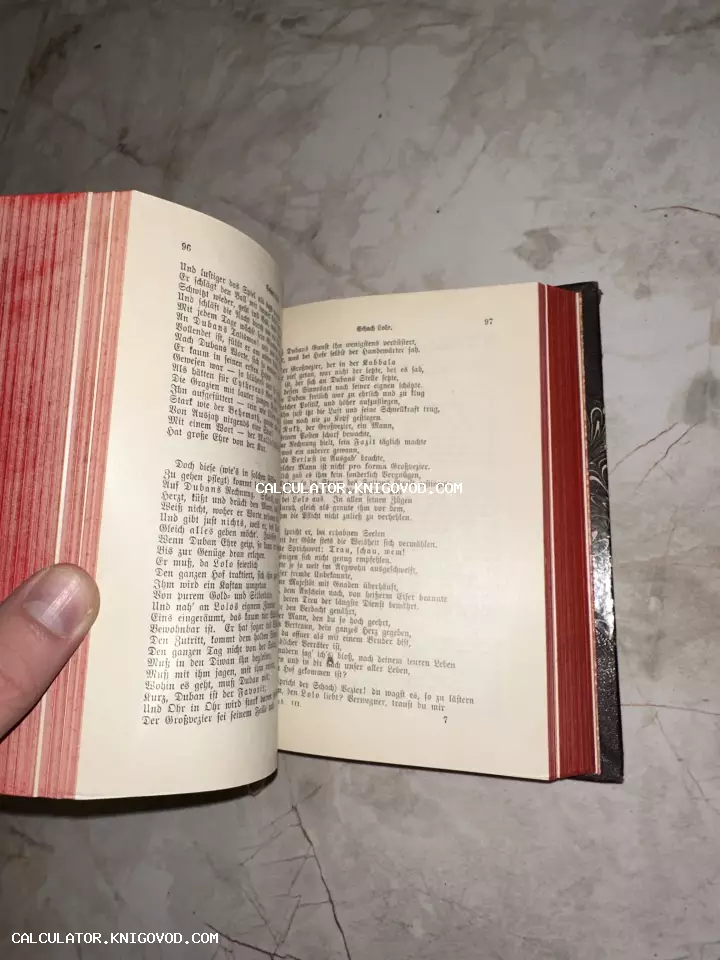 Раскрытая старинная книга с готическим шрифтом на страницах и ярко-красным боковым обрезом, лежащая на мраморной поверхности.