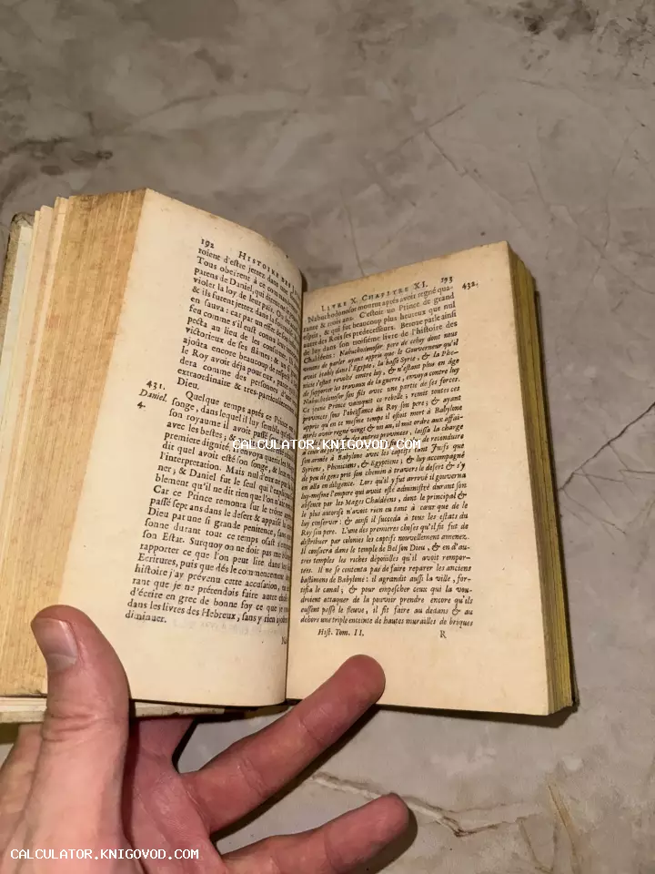 Раскрытая старинная книга с пожелтевшими страницами и французским текстом, которую держит рука человека на фоне мраморного пола.