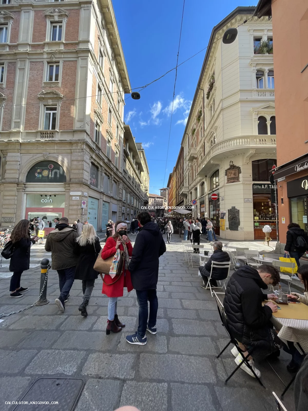 Вид на оживленную пешеходную улицу в историческом центре итальянского города с классической архитектурой, летними кафе и прохожими.