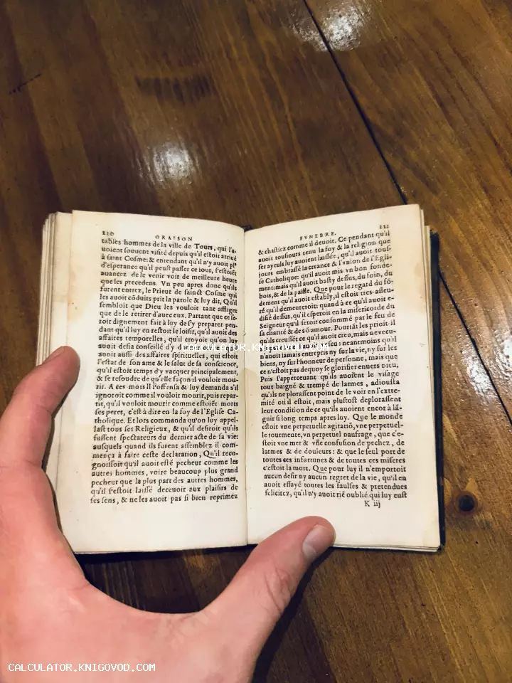 Раскрытая старинная книга на французском языке с заголовком Oraison Funebre, которую держат в руках на фоне деревянного стола.
