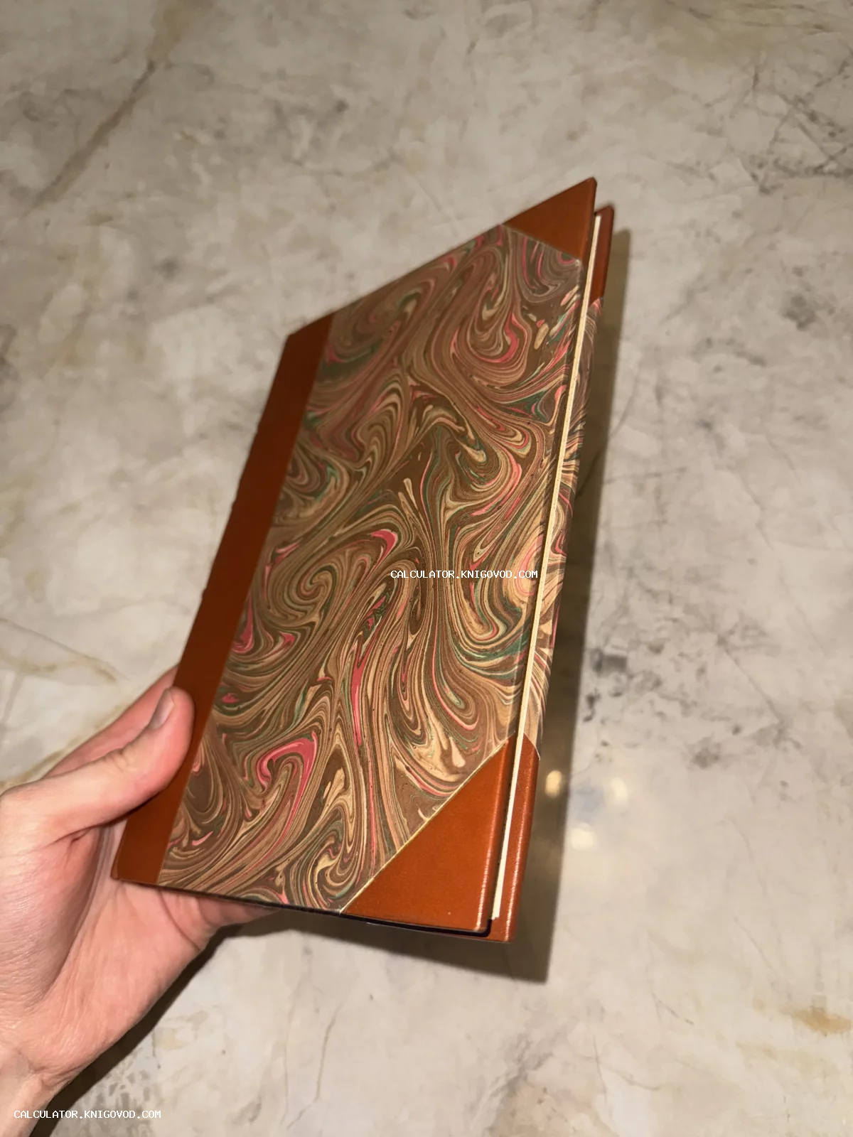 Книга в твердом переплете с коричневыми кожаными уголками и корешком, украшенная декоративной мраморной бумагой с вихревым узором.