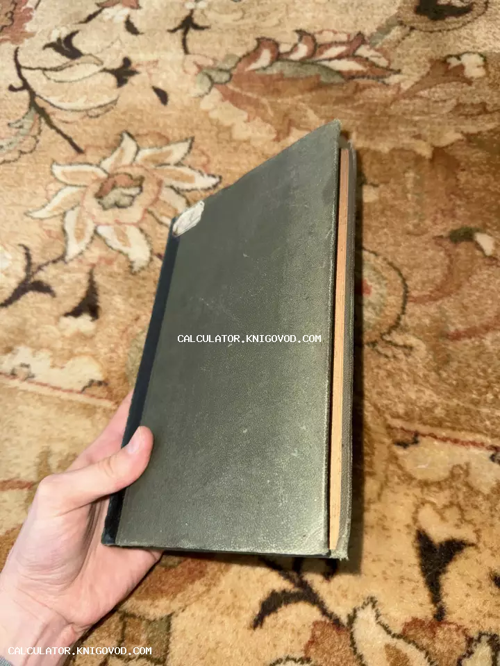 Старая книга с темно-зеленой текстурной обложкой и пожелтевшими страницами в руке на фоне ковра.