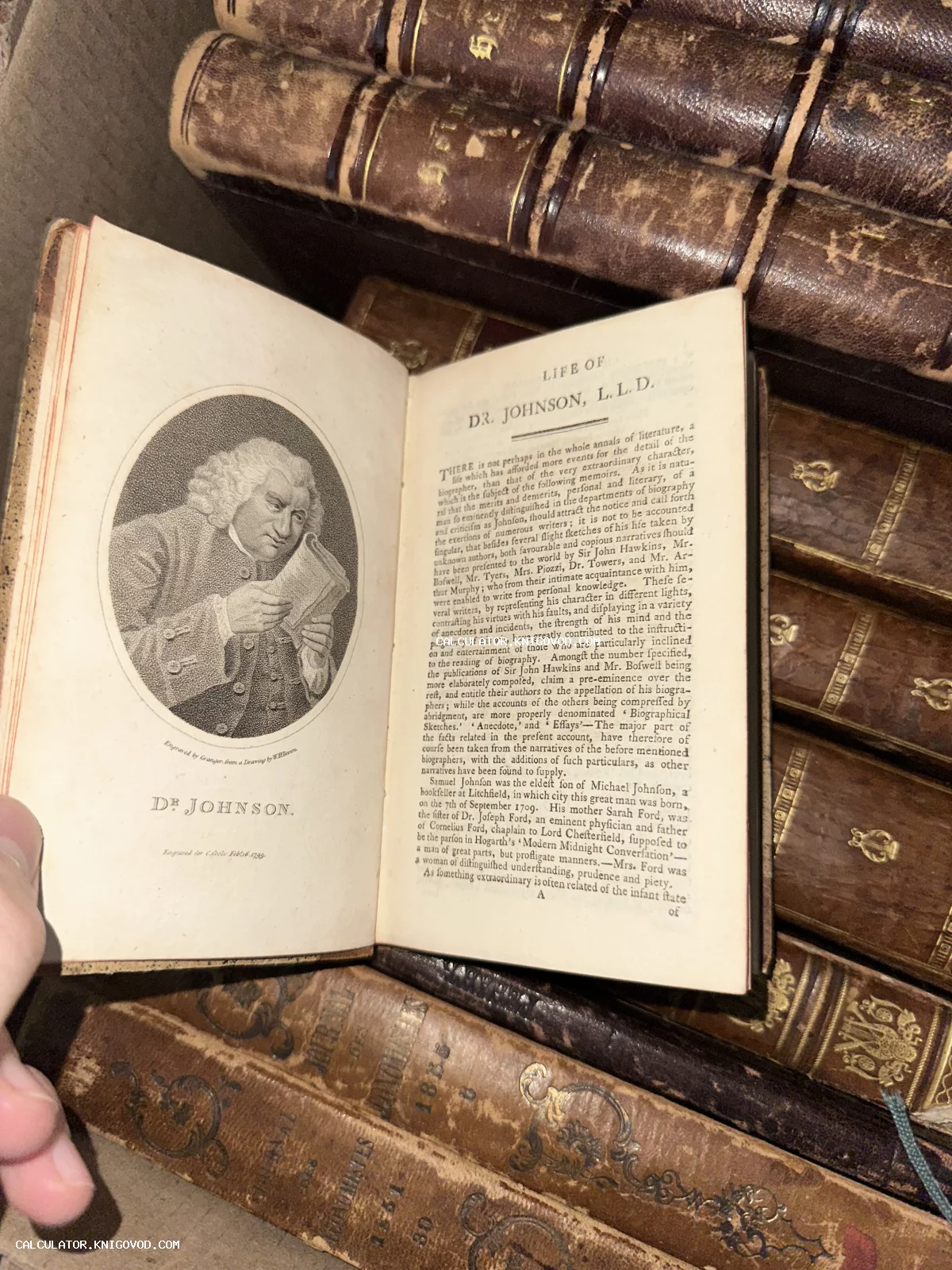 Разворот старинной книги с гравированным портретом Сэмюэла Джонсона и текстом на фоне стопки книг в кожаных переплетах.