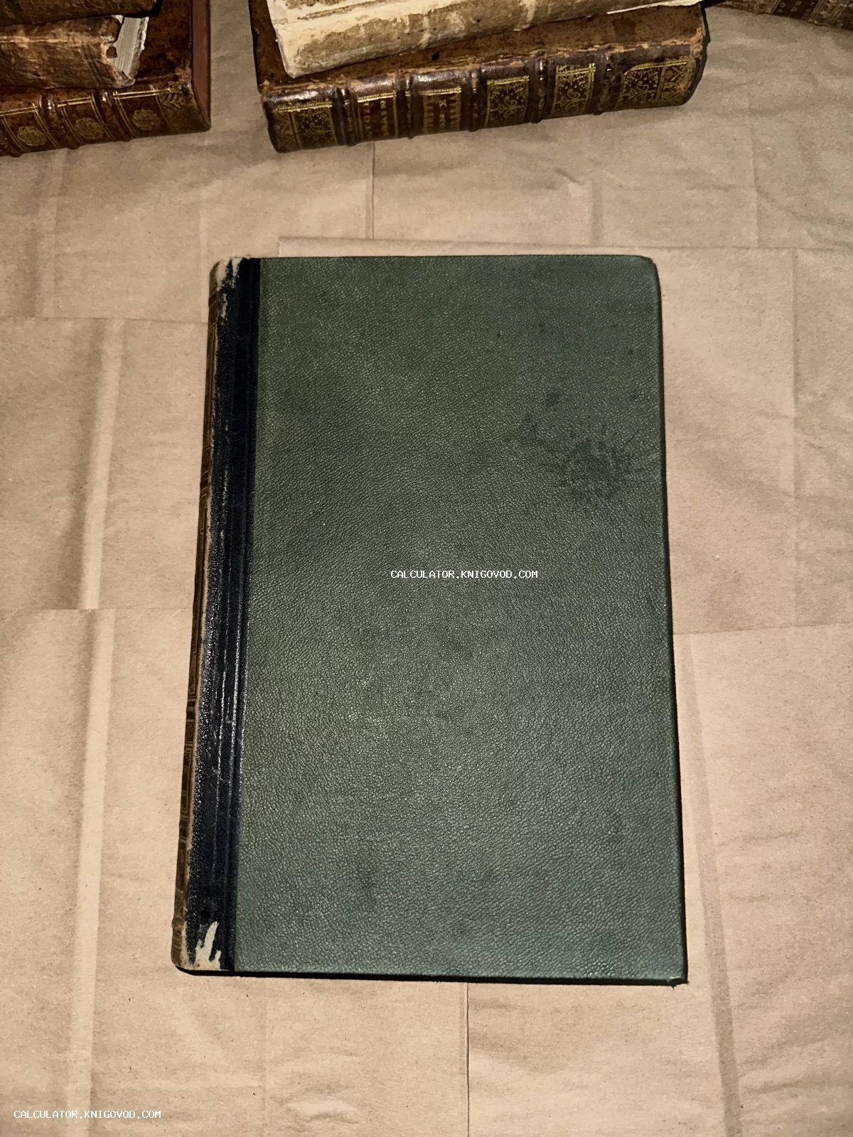 Старинная книга с фактурной зеленой обложкой и потертым черным корешком на фоне крафтовой бумаги.