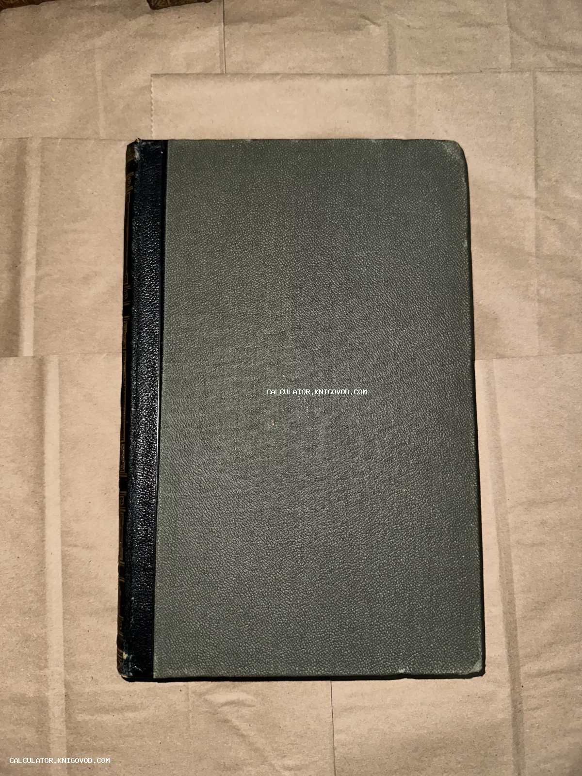 Старинная книга с темно-синим кожаным корешком и серой фактурной обложкой на коричневой бумаге.