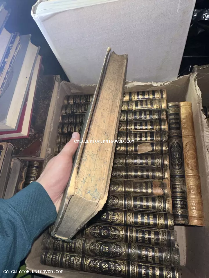 Рука держит старинную книгу с мраморным обрезом на фоне множества томов в кожаных переплетах с золотым тиснением.