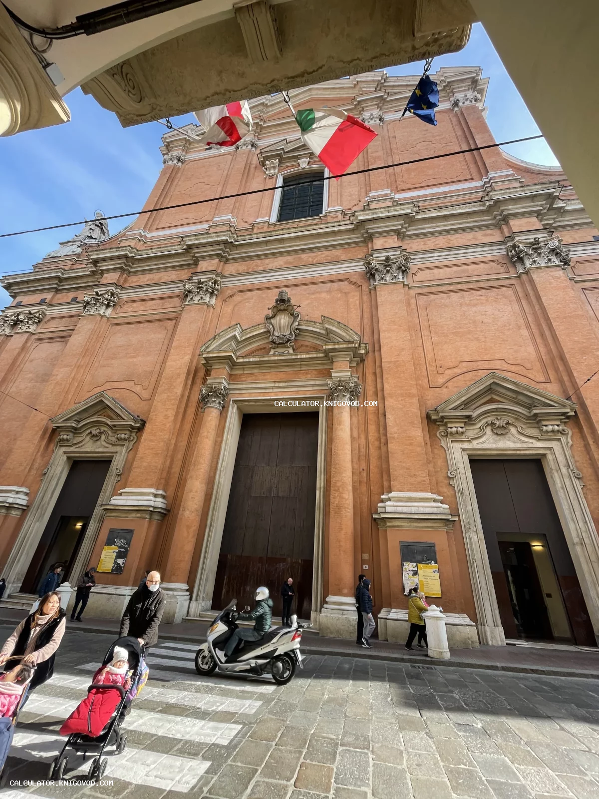 Терракотовый фасад итальянского собора в стиле барокко с колоннами, тремя порталами и флагами над входом.