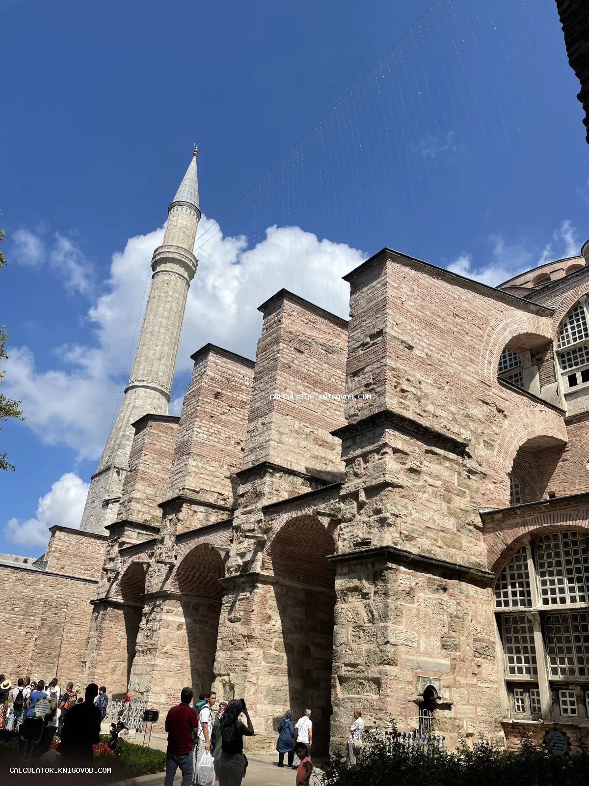 Вид снизу на массивные каменные контрфорсы и минарет собора Святой Софии в Стамбуле на фоне синего неба.