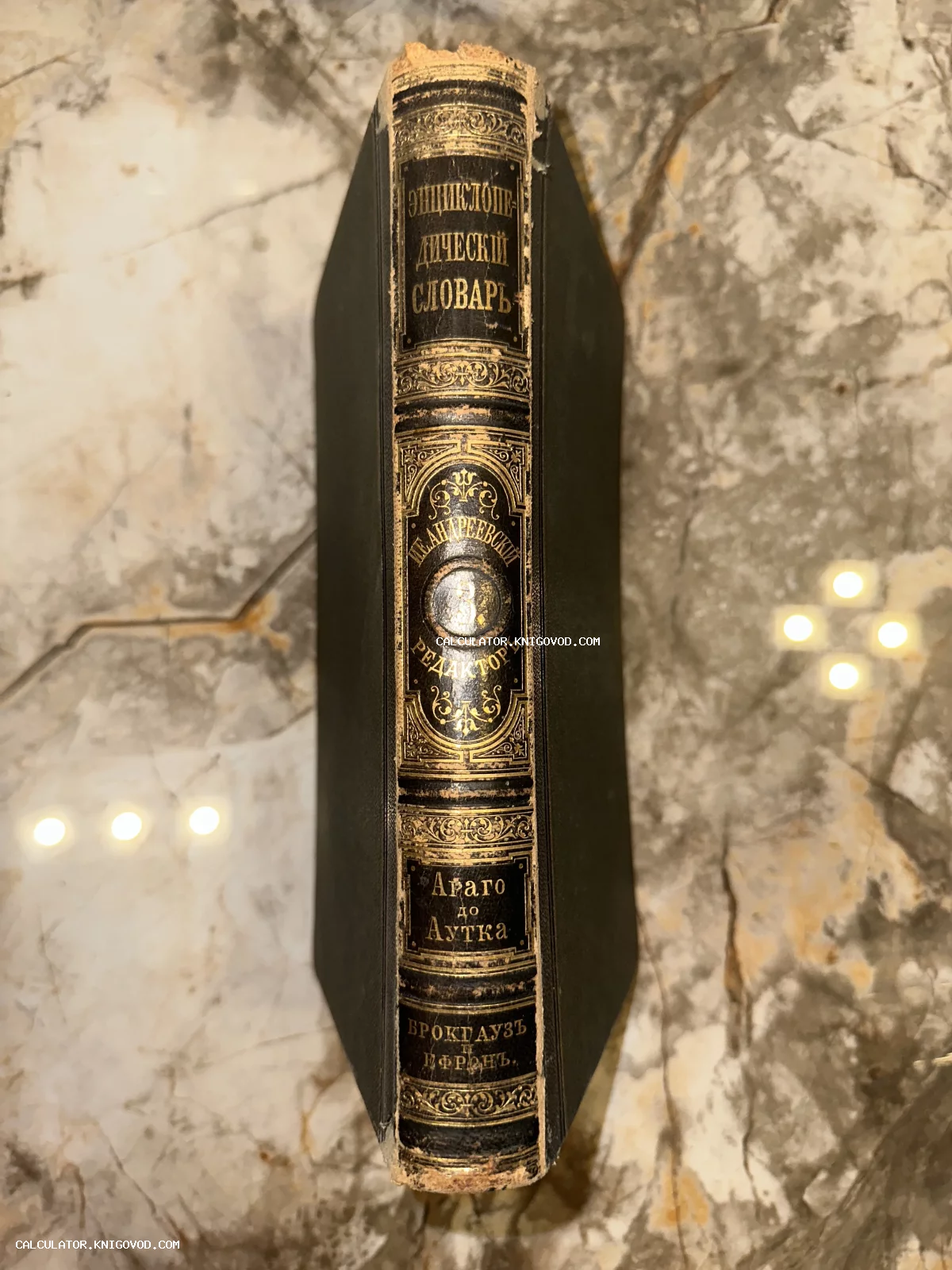 Корешок антикварной книги в кожаном переплете с золотым тиснением на фоне мрамора