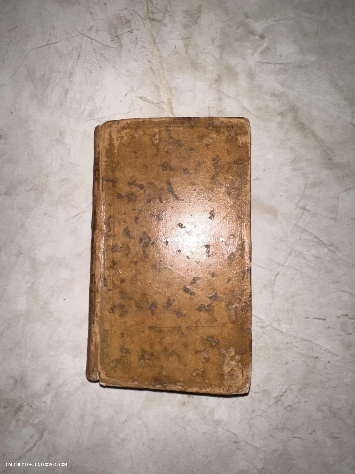 Старинная карманная книга с потертым коричневым кожаным переплетом на светлом мраморном фоне.