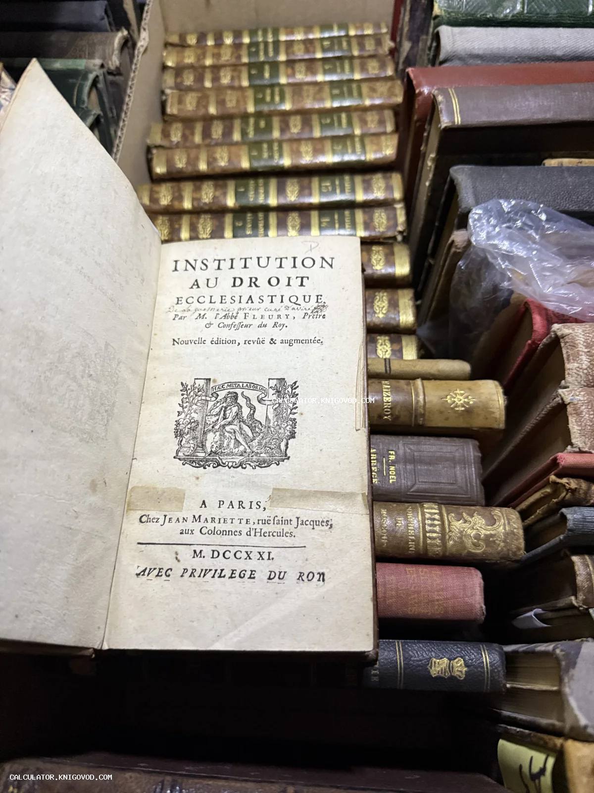 Раскрытая антикварная книга XVIII века с гравюрой на титульном листе среди множества старинных кожаных переплетов.