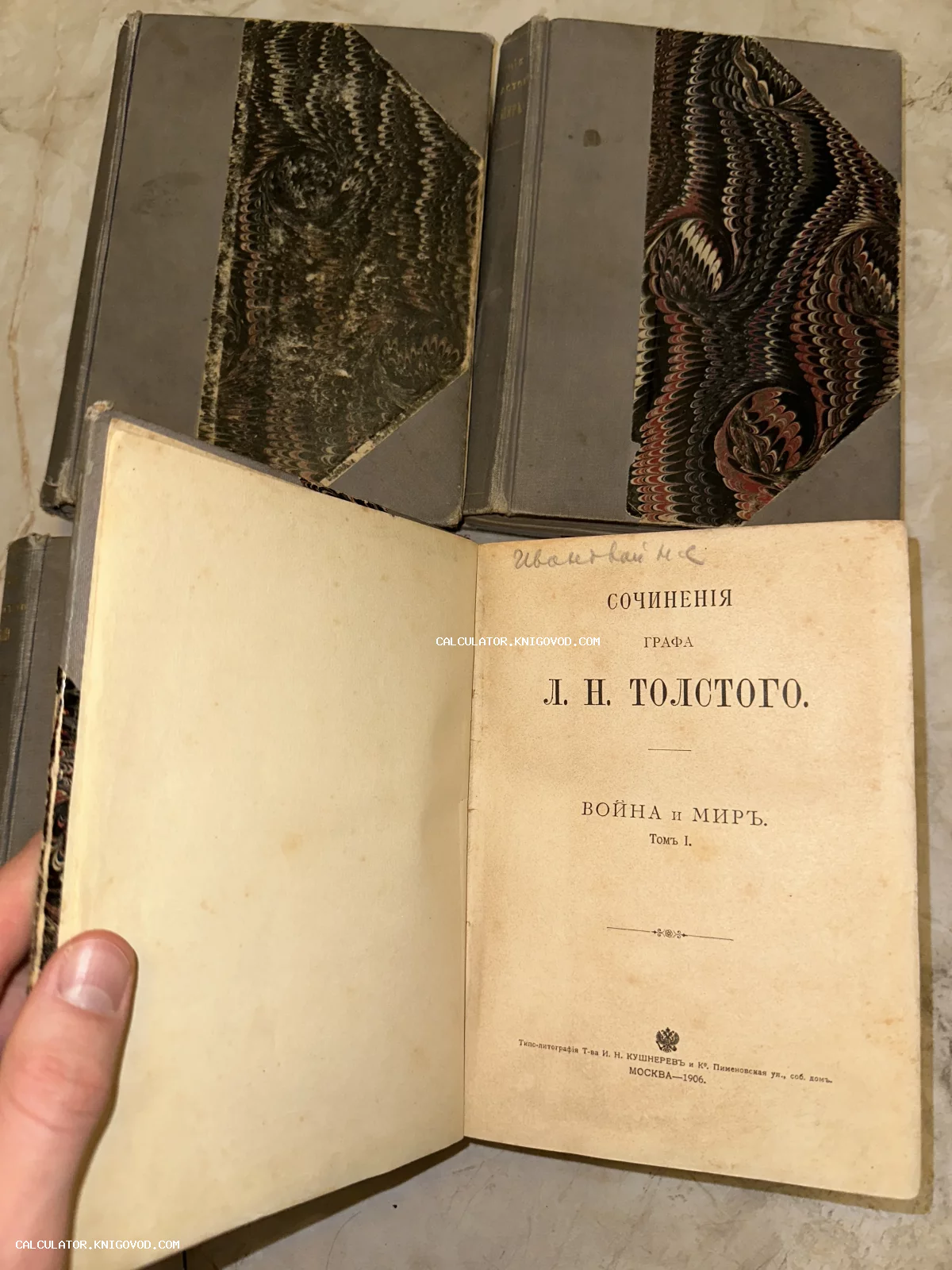 Раскрытый антикварный том романа Толстого «Война и мир» 1906 года издания на фоне книг с мраморным переплетом.