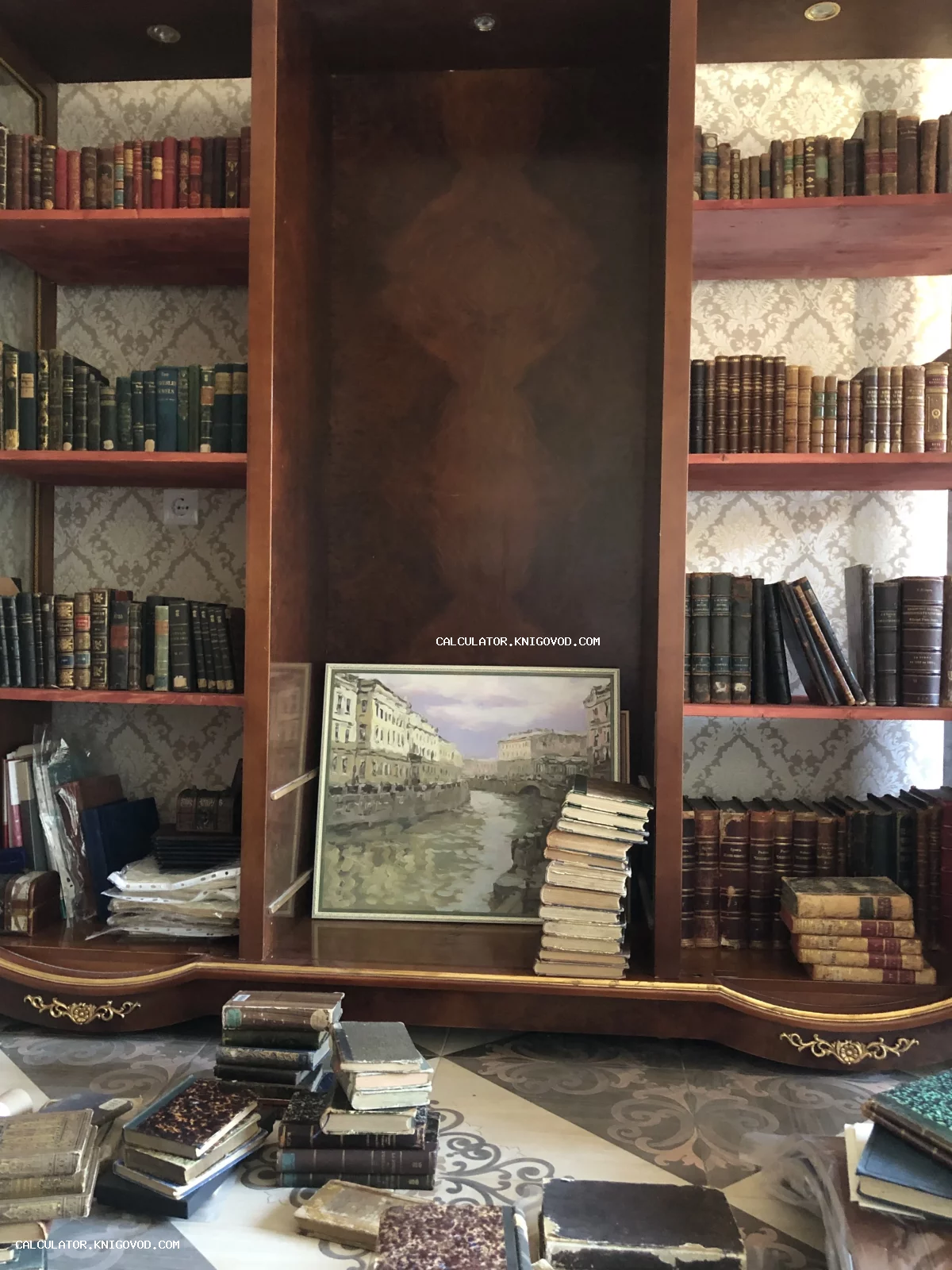 Массивный деревянный стеллаж, заполненный старинными книгами в кожаных переплетах, со стопками книг на полу и картиной с видом на канал.