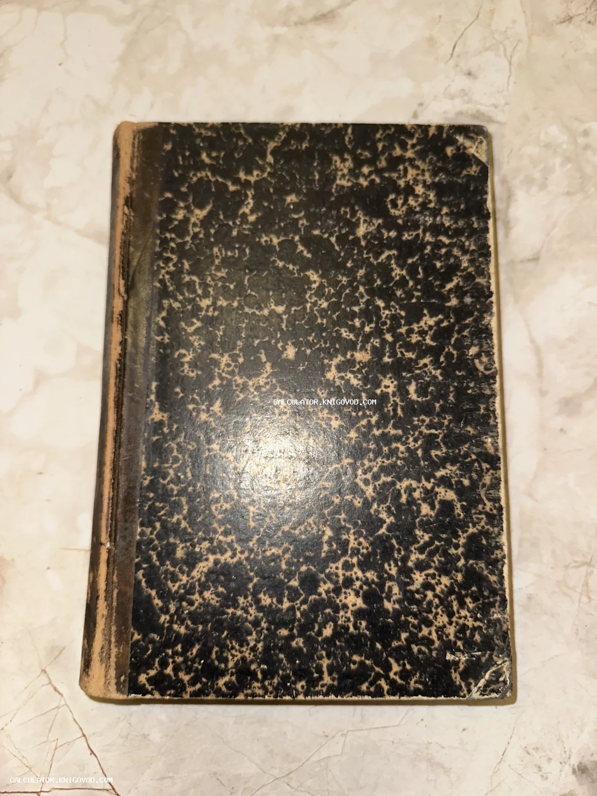 Старинная книга с темной обложкой и желтоватым мраморным узором, потертый корешок, вид сверху.