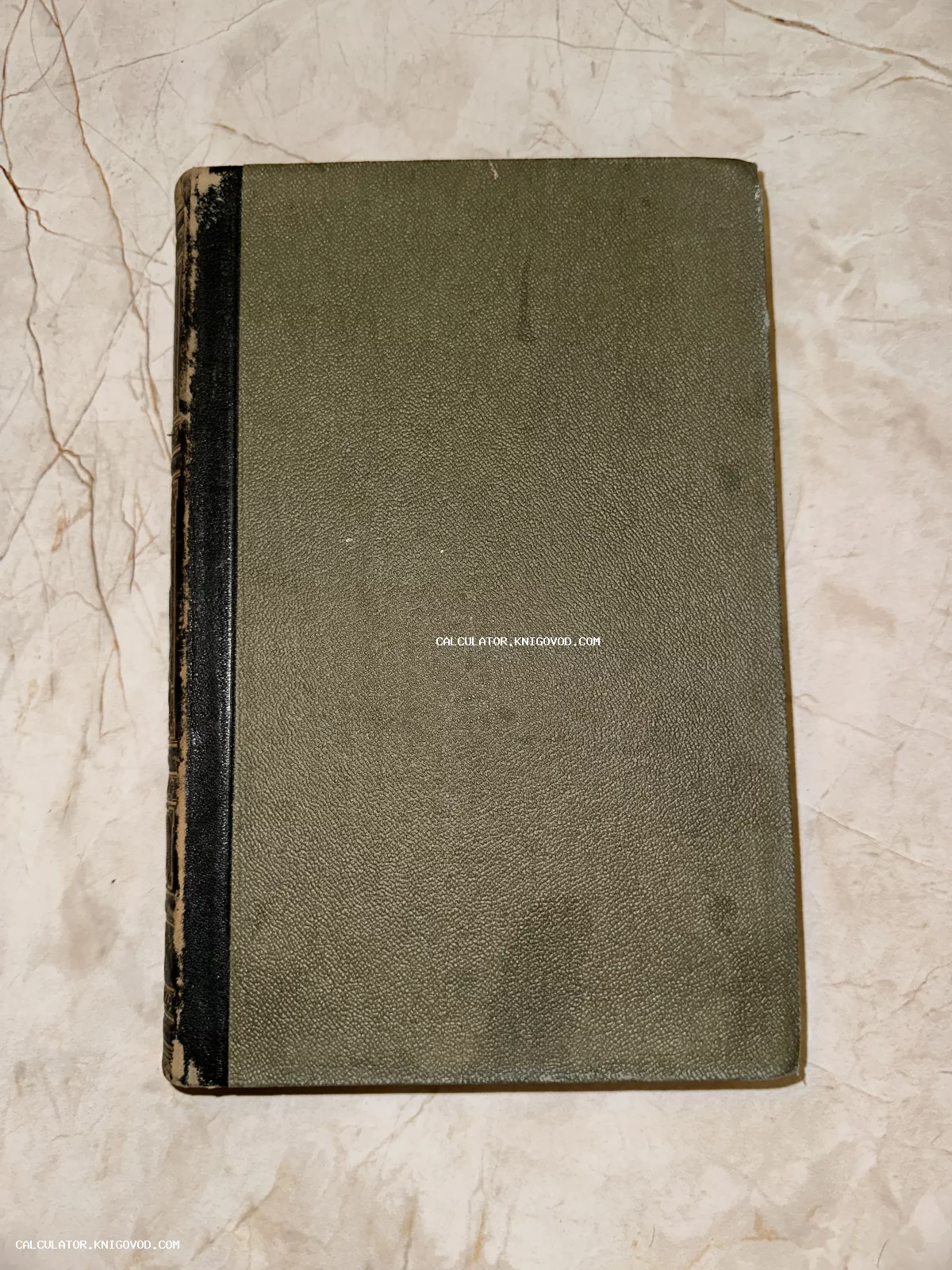 Антикварная книга с текстурированной зеленой обложкой и черным корешком на светлом фоне
