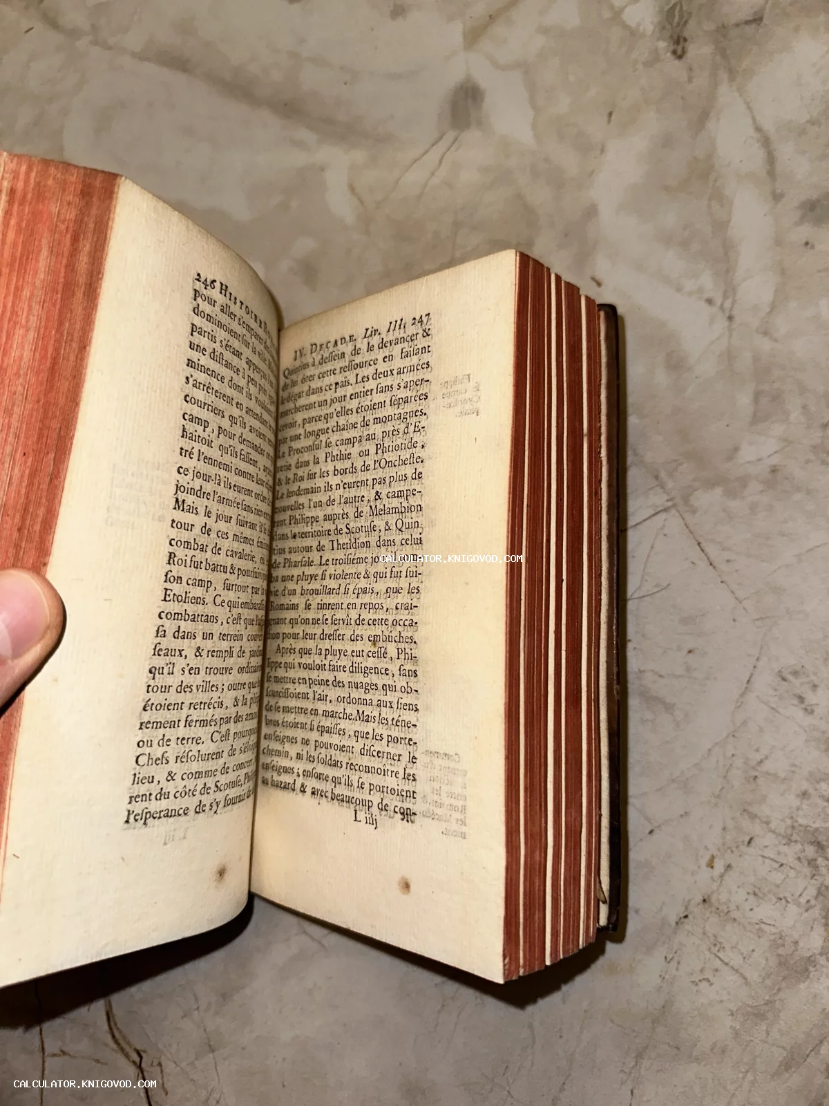 Открытая антикварная книга с французским текстом, пожелтевшими страницами и красным обрезом на мраморном фоне.